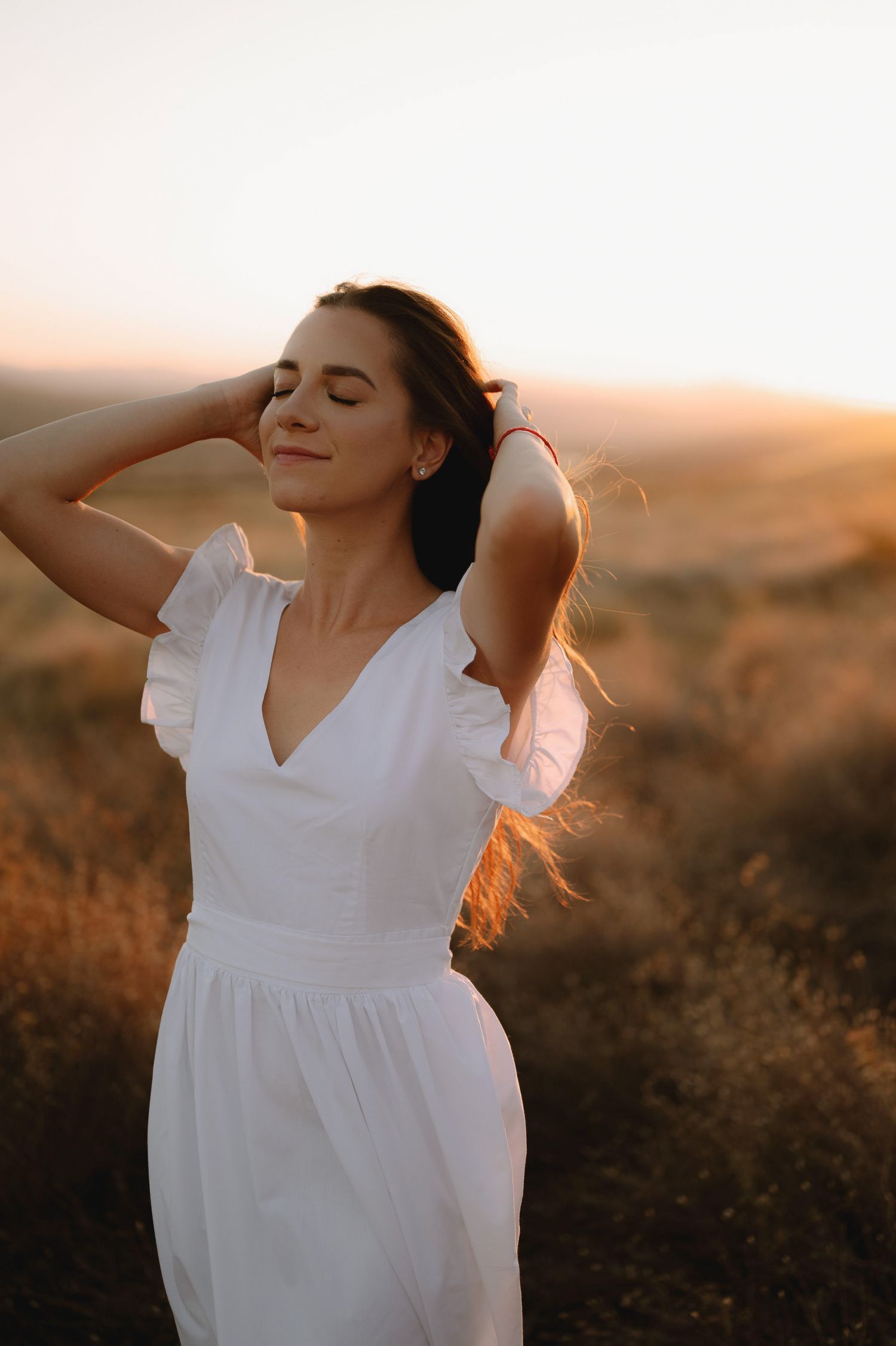 A woman in a flowing white dress dances gracefully in a golden field at sunset.