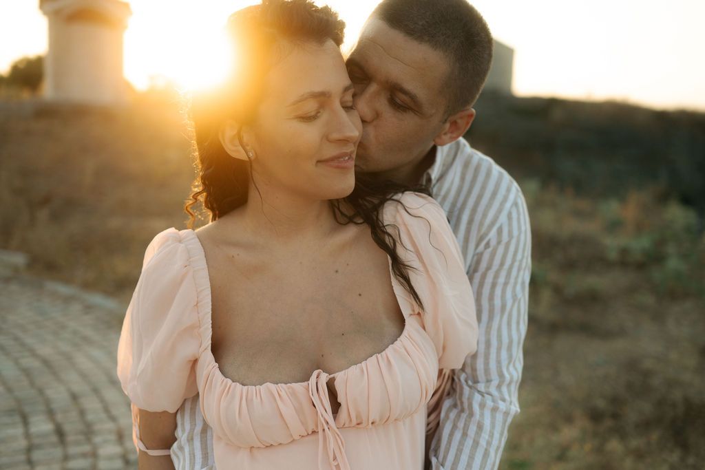 Romantic couple embraces during golden hour sunset in a rustic outdoor setting.
