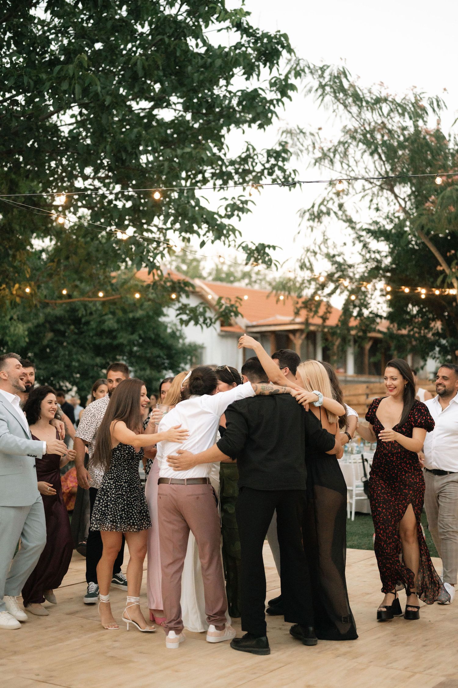 A group of wedding guests dance together in a line formation outdoors during a reception celebration.
