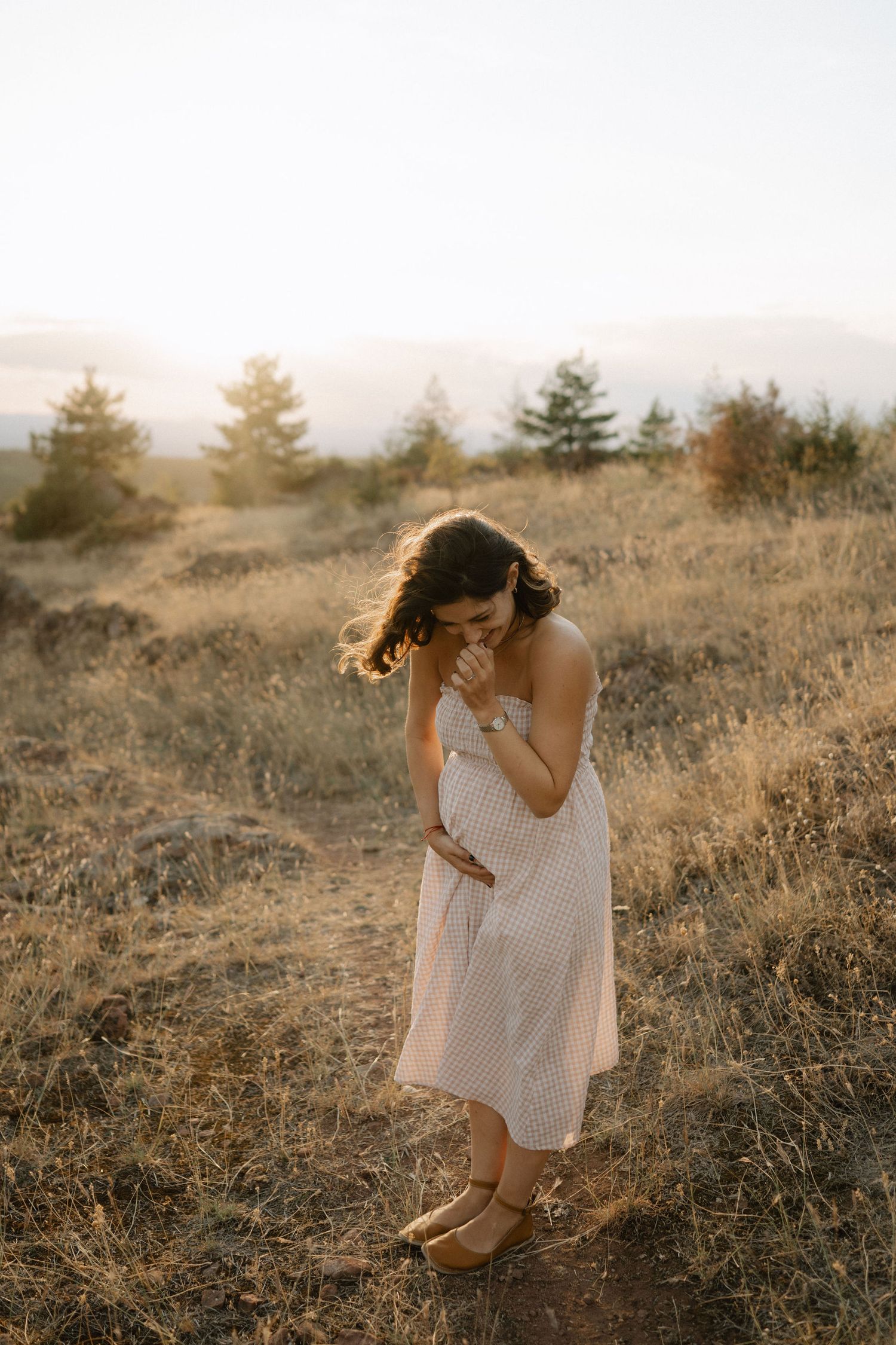 A figure in a flowy white dress poses gracefully in a sunlit field of dried grass at golden hour.