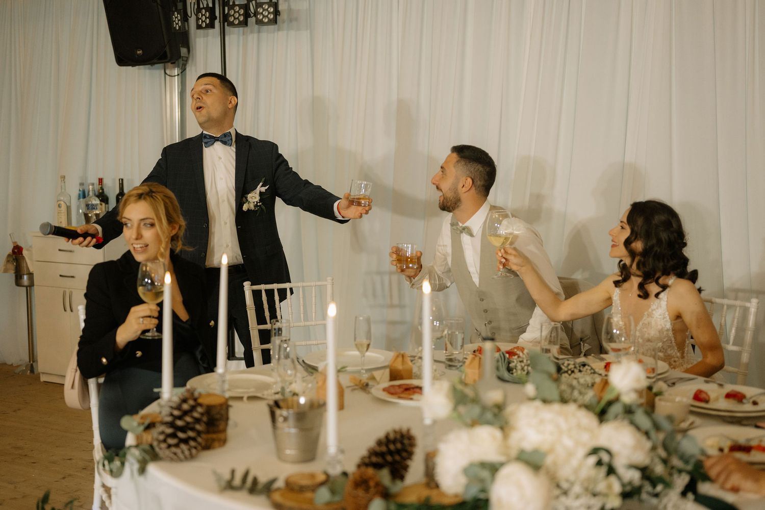 Elegant wedding reception toast with guests raising glasses around a candlelit table with floral centerpieces.