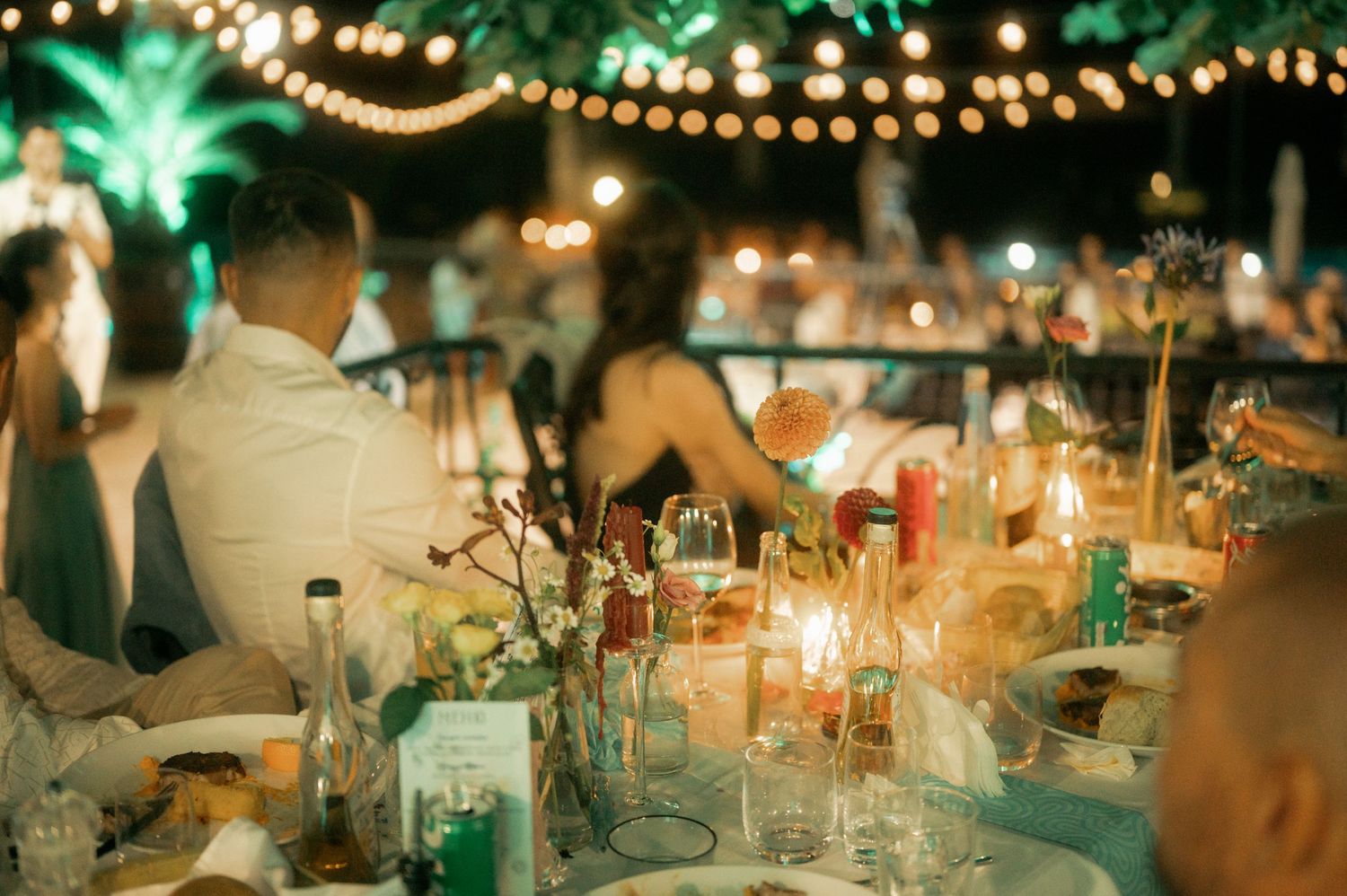 Elegant wedding reception table setting with glowing candles and string lights creating a romantic atmosphere.