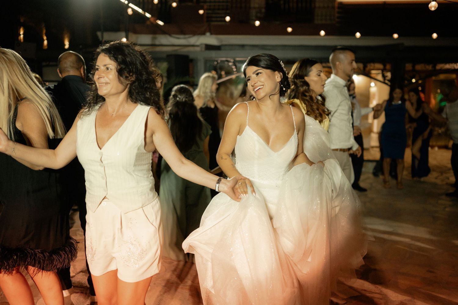 A group of dancers in white dresses perform together on a dance floor at a social gathering.