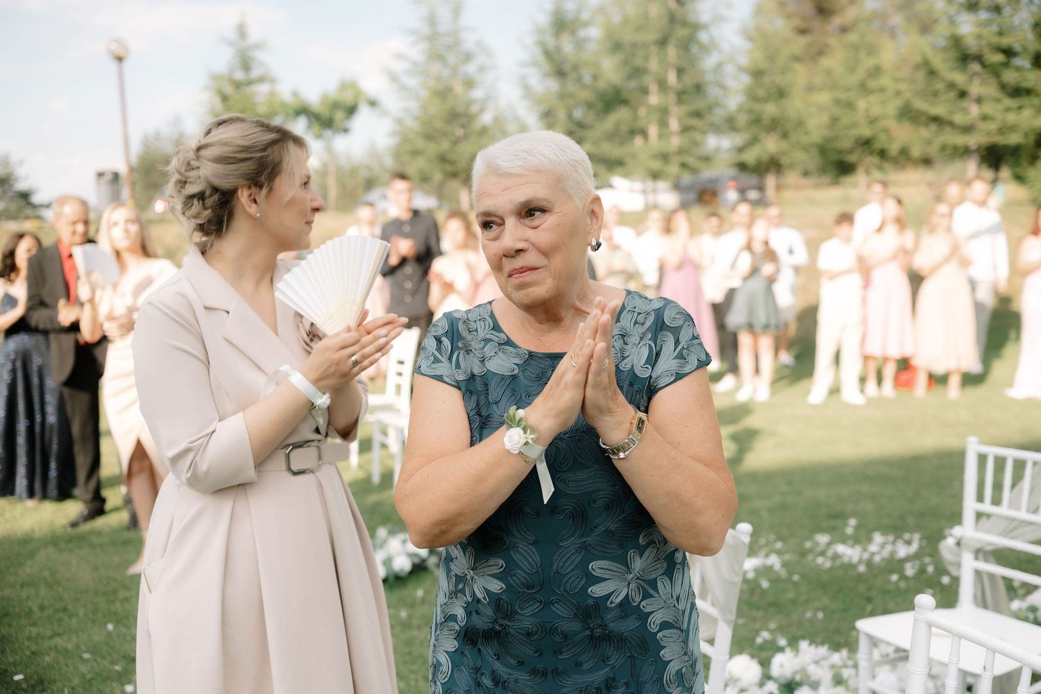 Wedding guests stand and applaud during an emotional outdoor ceremony on a sunny summer day.