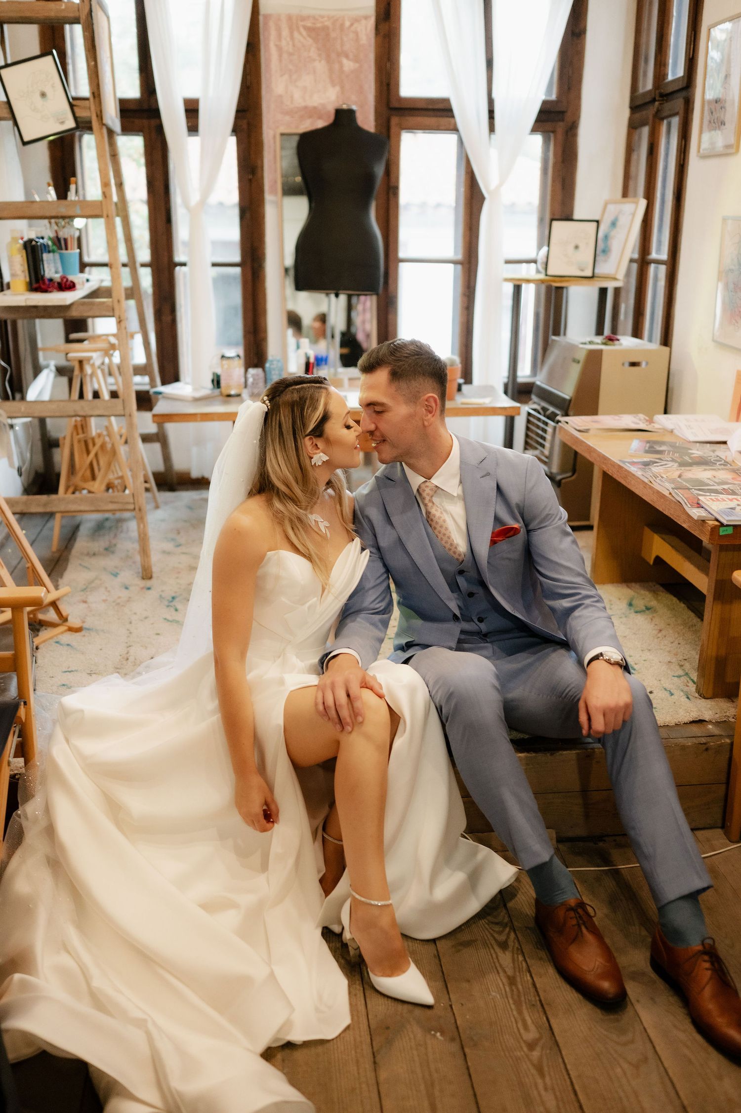Newlyweds in white dress and grey suit share tender moments while seated on vintage wooden benches.