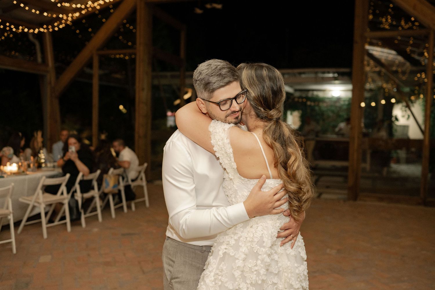 A romantic first dance between newlyweds in a rustic barn venue illuminated by warm string lights.