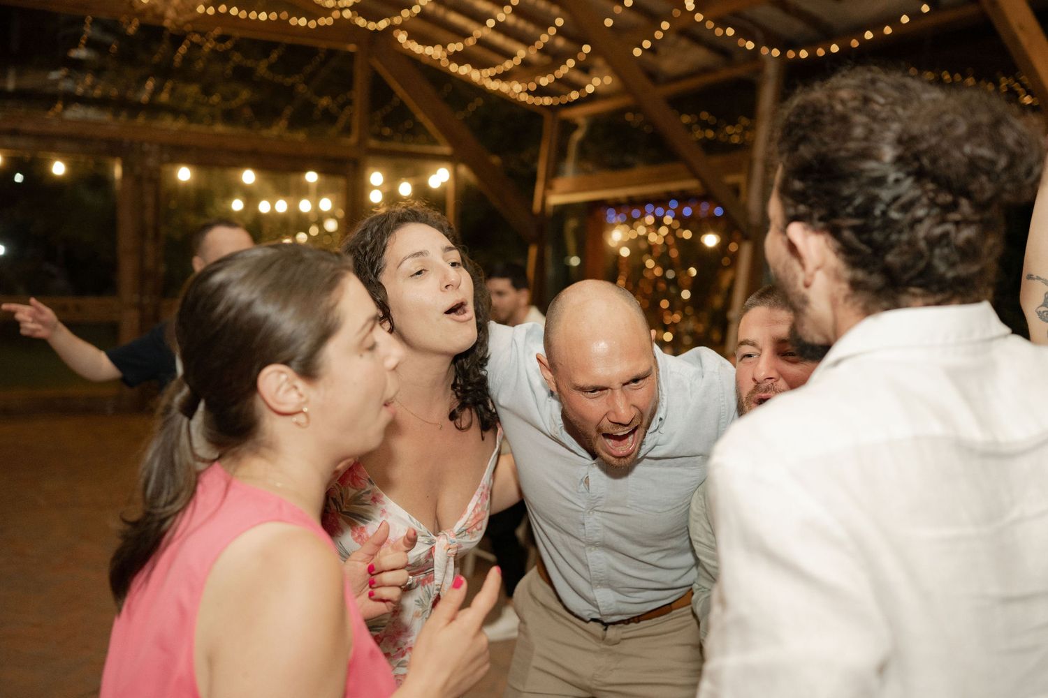 A group of party guests laugh enthusiastically together during a celebration under decorative lighting.