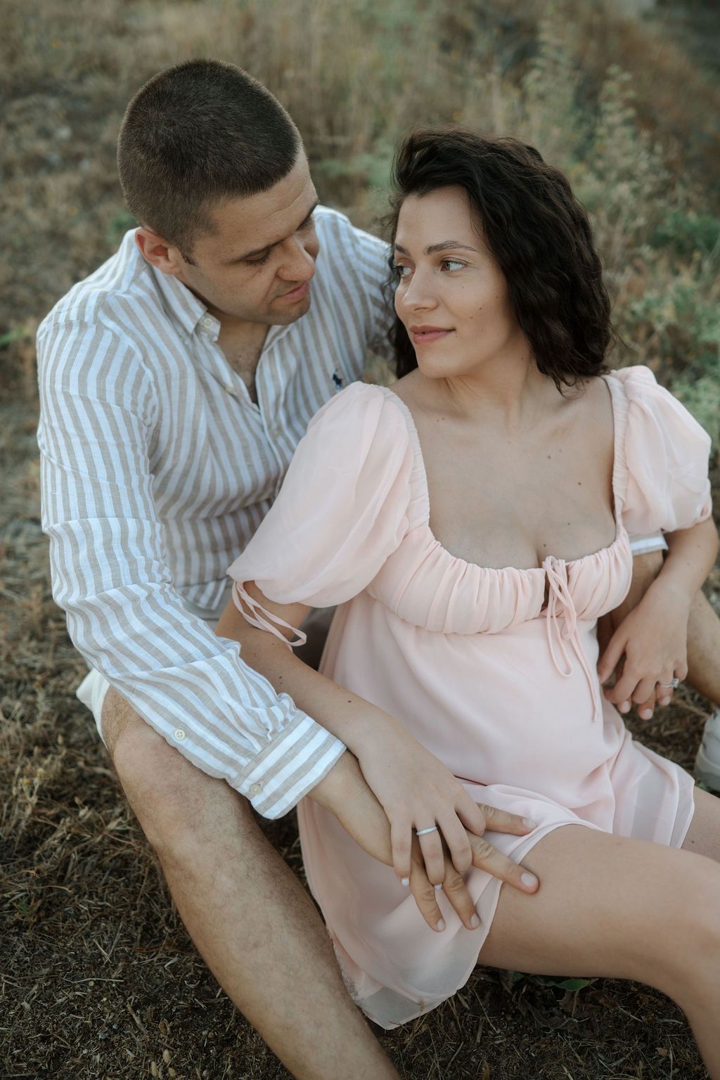 A couple in a pink dress and striped shirt share intimate moments outdoors in a romantic photoshoot series.