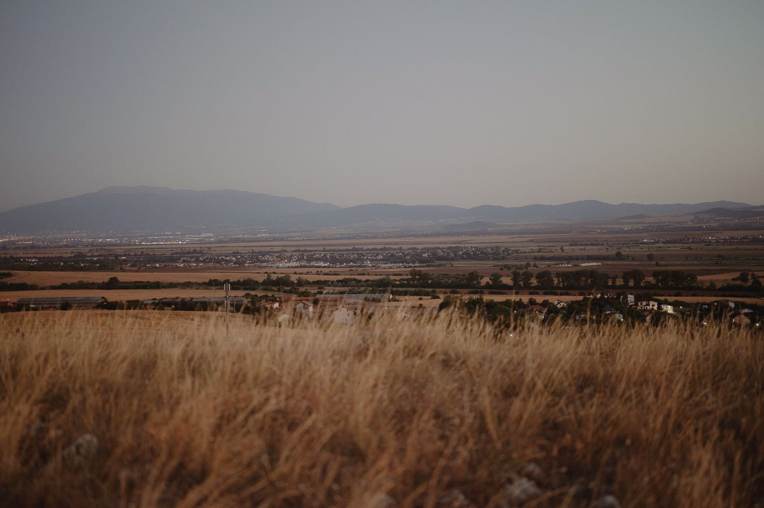 Expansive grassland prairie landscape with distant mountains and dry golden grass swaying in the foreground.