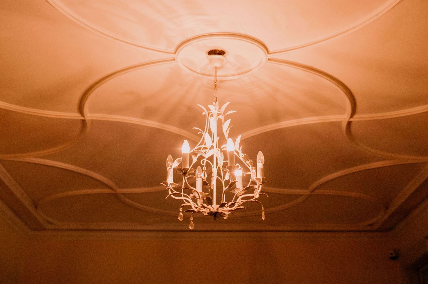 Elegant crystal chandeliers illuminate an ornate ceiling with decorative molding in warm amber lighting.