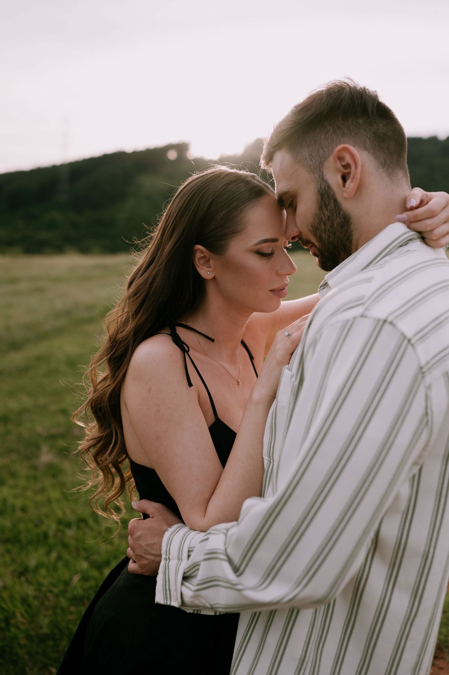 A romantic couple shares intimate moments in a field during a sunset photoshoot.
