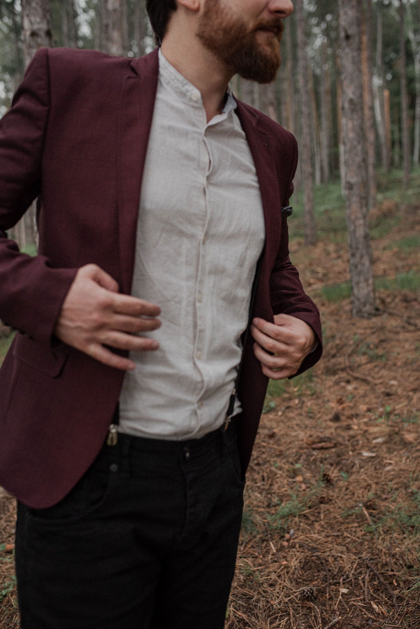 A burgundy suit jacket and white dress shirt combination shown in a forest setting against pine trees.
