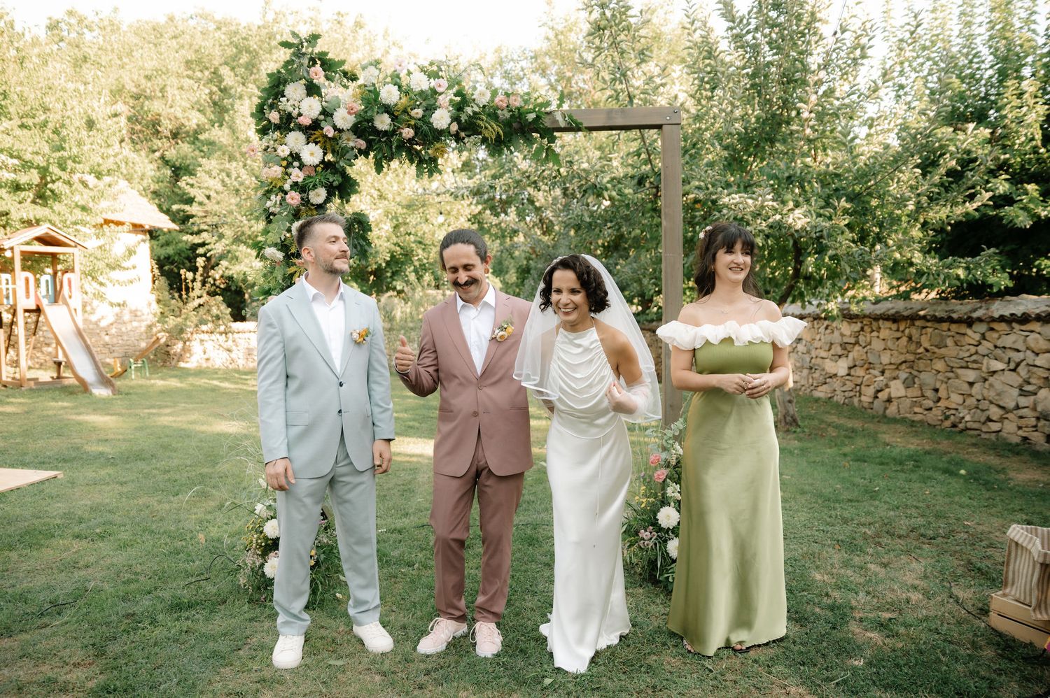 A group of people in coordinated pastel outfits pose together in a garden setting during a celebration.