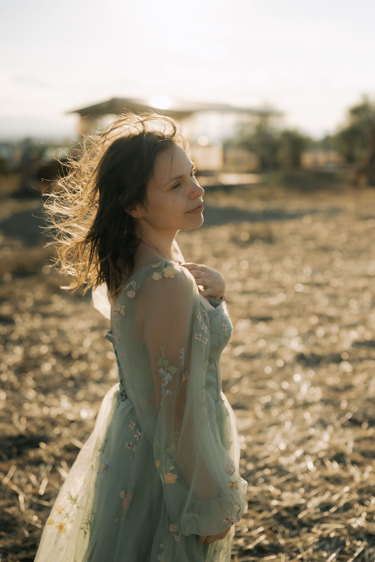 A person in a flowy blue dress twirls joyfully in a sunlit field during golden hour.