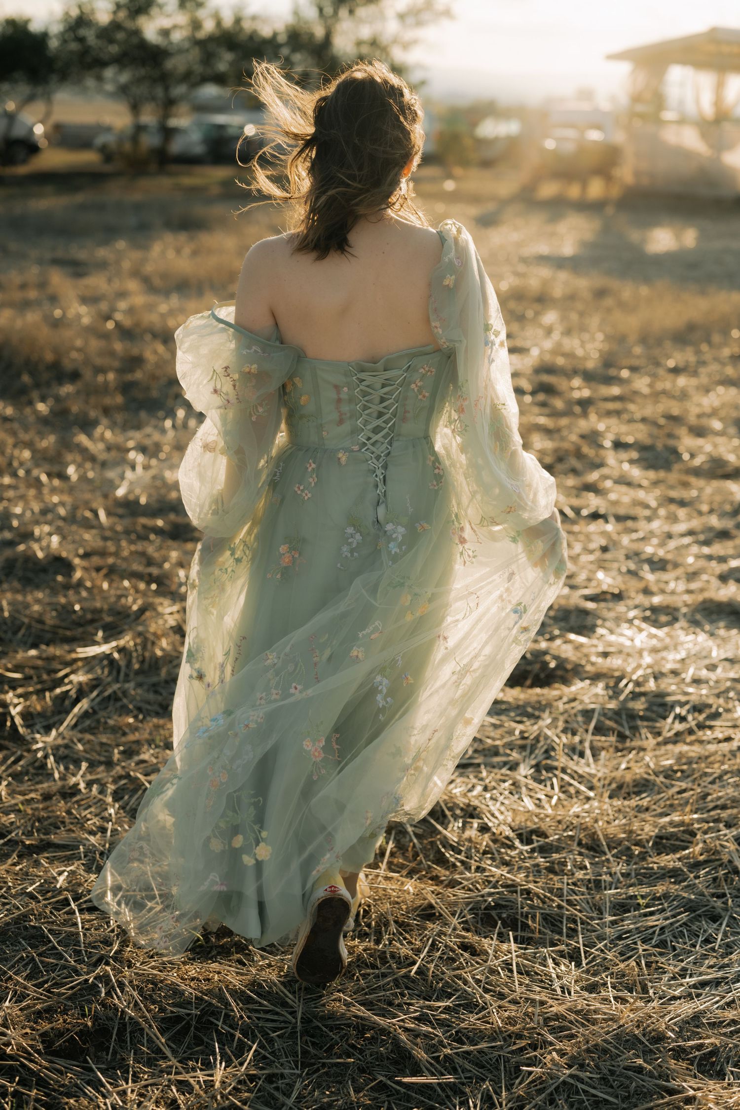 A person in a flowing vintage lace dress runs through a sunlit field at golden hour.