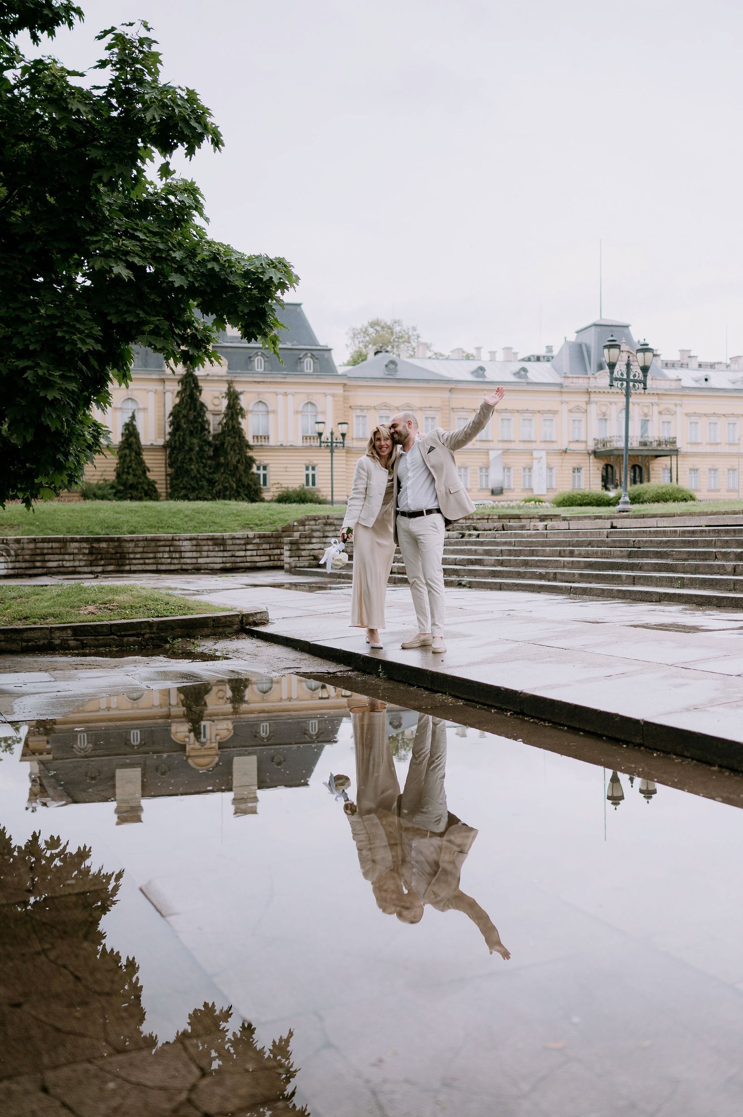 Dancing figures create reflections in a pool outside a grand historic building.