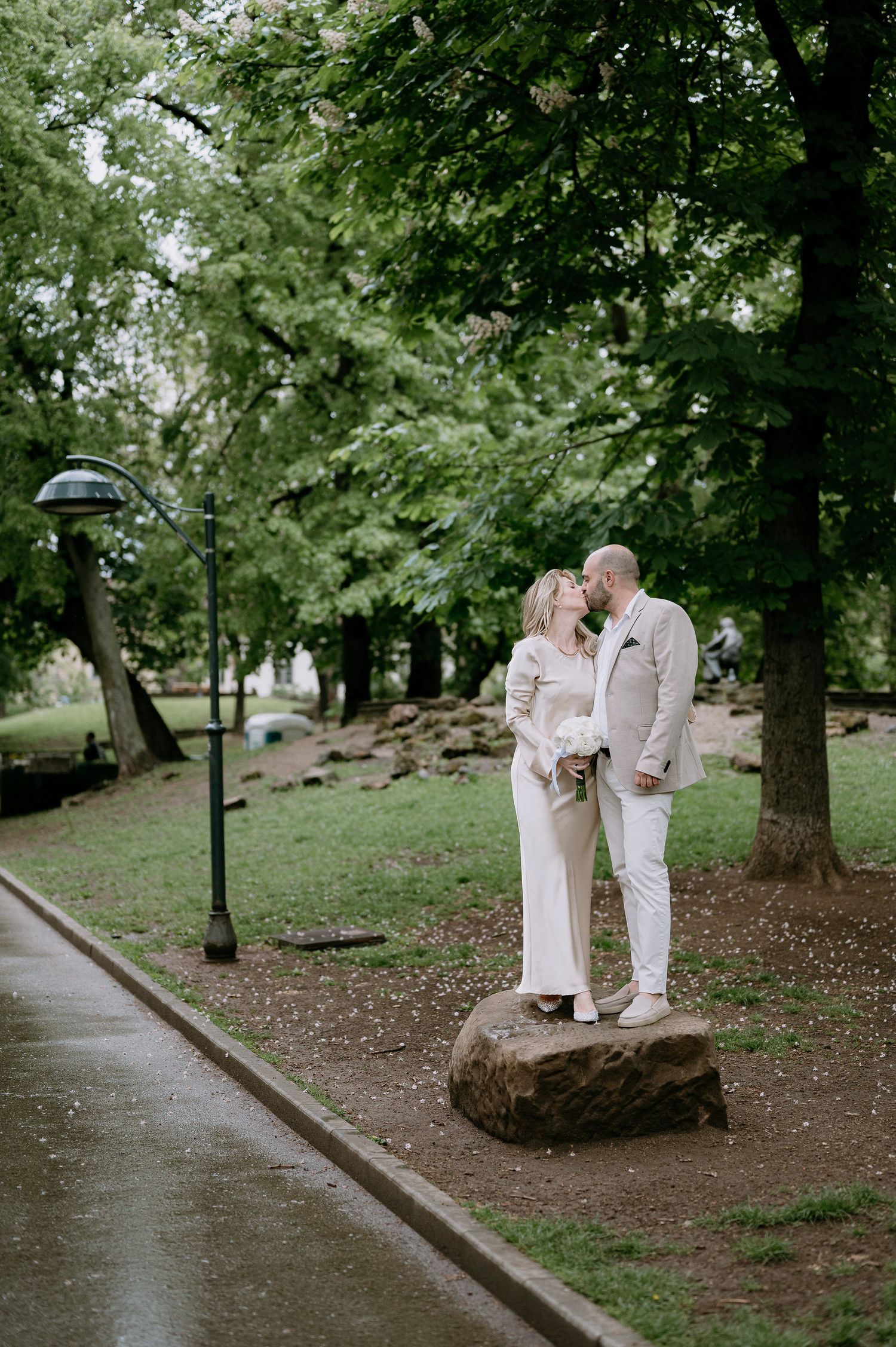A couple shares an intimate moment while standing on a large rock in a green park.