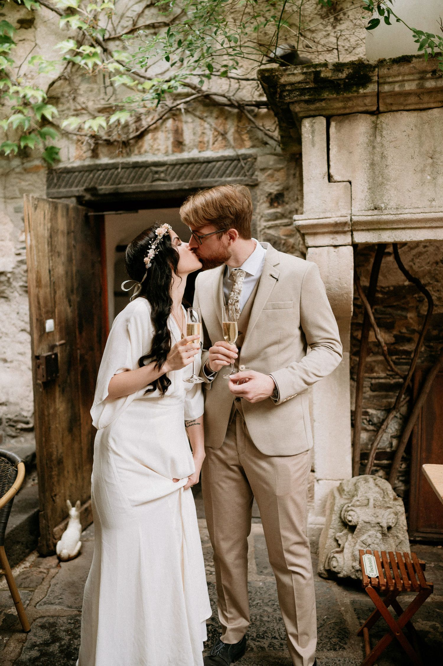 Newlyweds share champagne and laughter in a charming outdoor courtyard setting.