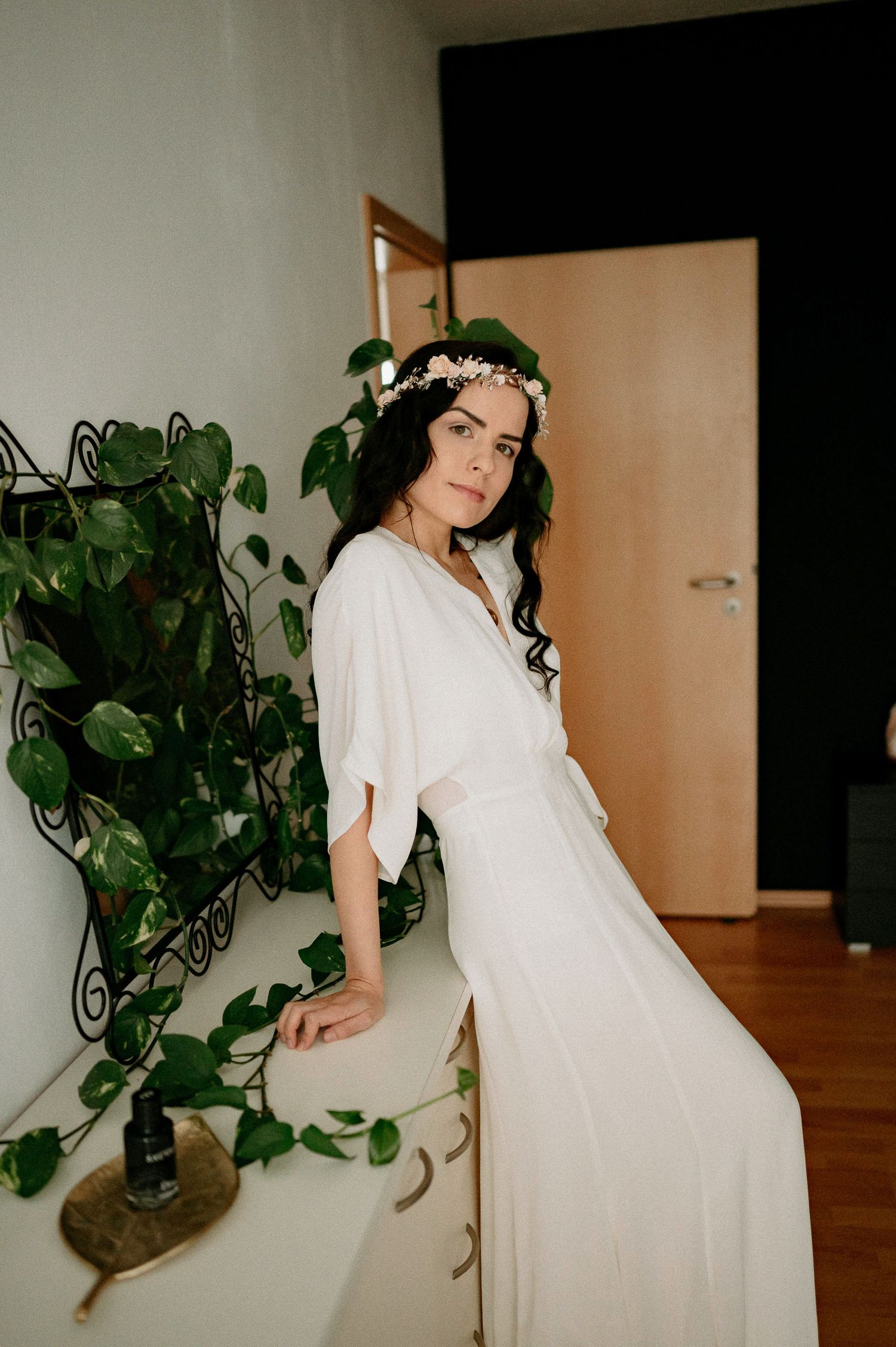 Dreamy indoor photoshoot with white dress and potted plants creating natural ambiance.