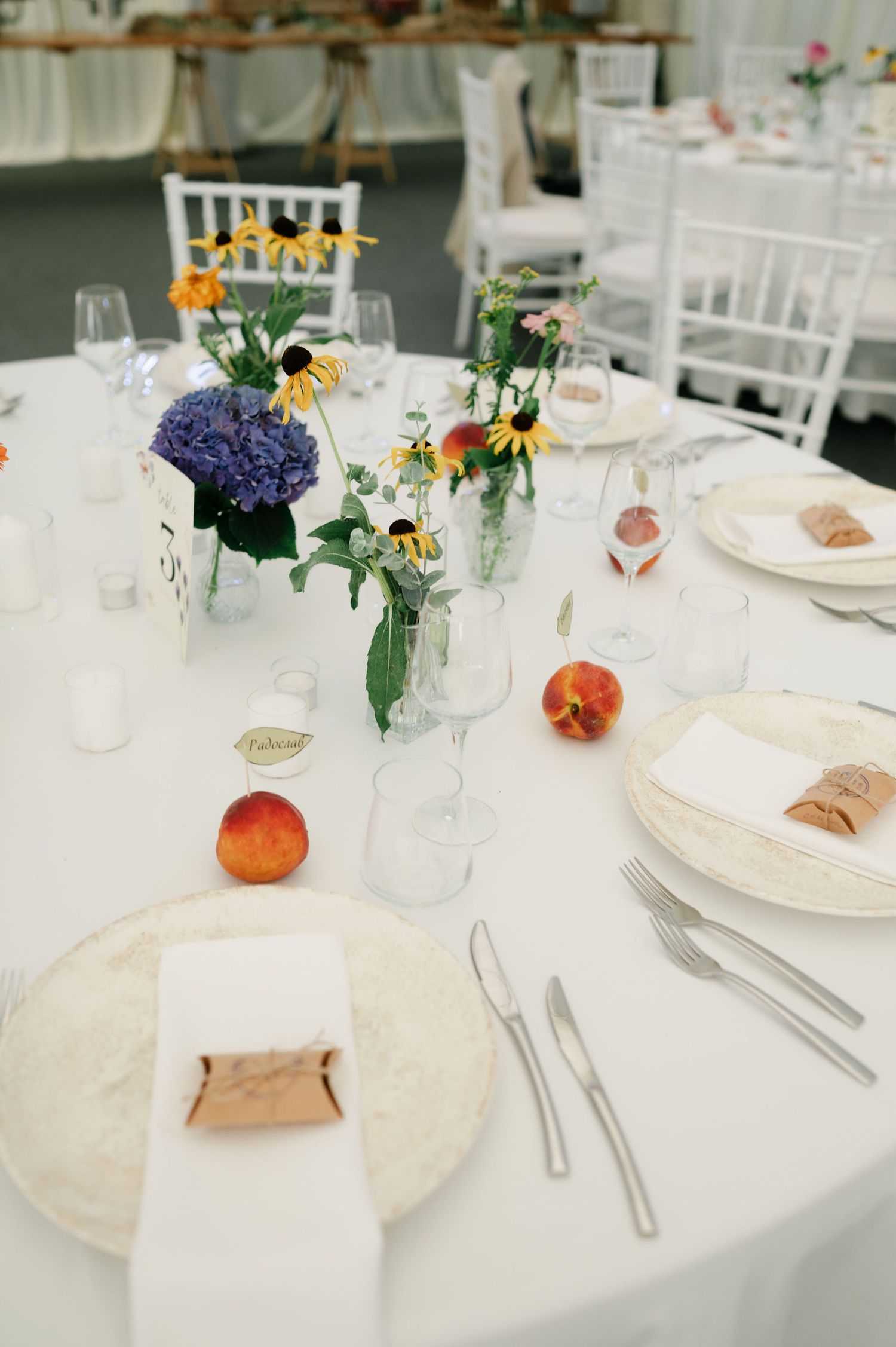 Wedding reception table with white linens, fresh flowers in glass vases, and peach accents.