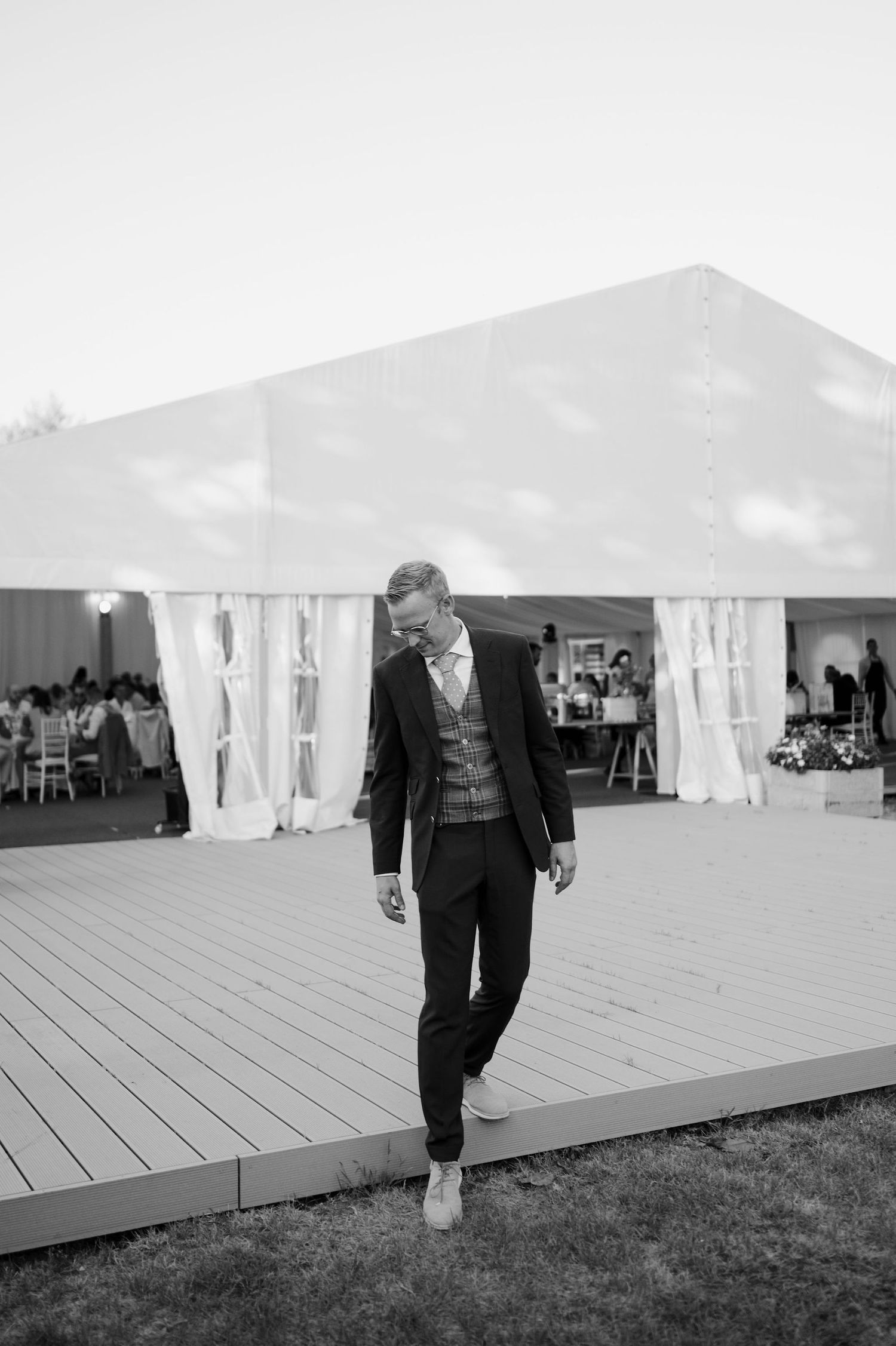A person walking along a wooden deck platform with large white event tents visible behind.