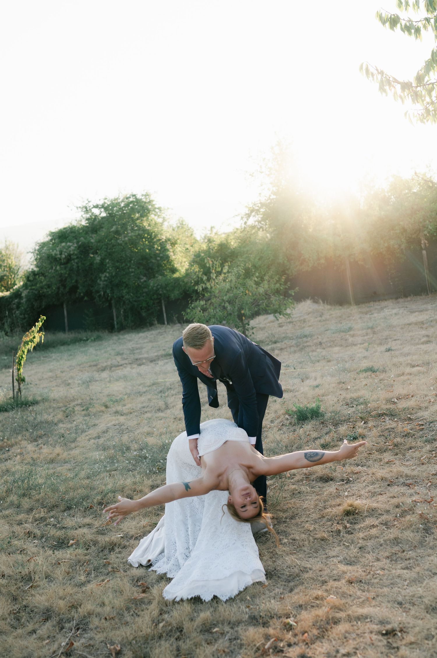 Newlyweds perform a dramatic dance dip pose against a sunset backdrop.