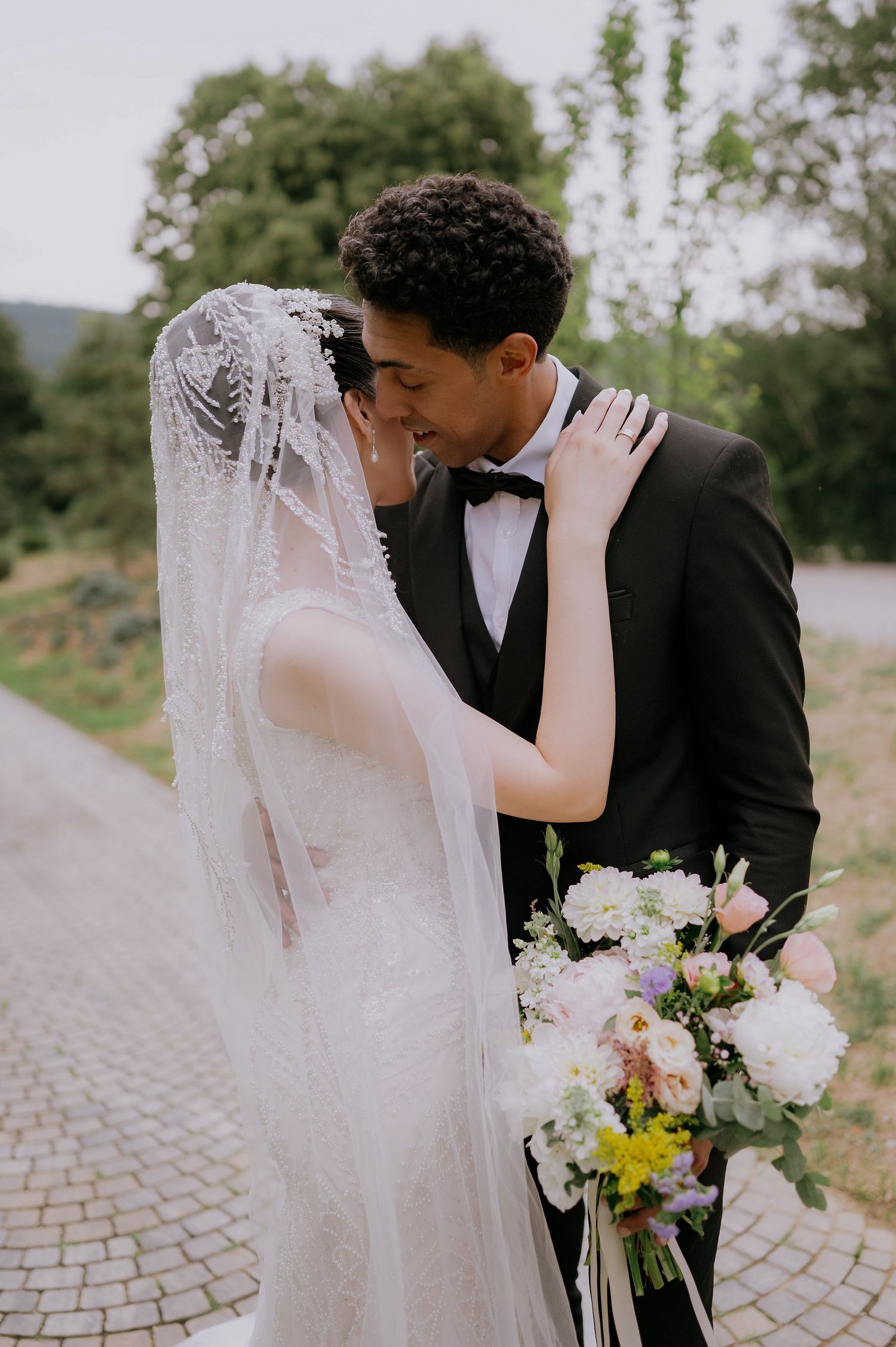 Intimate wedding portraits with delicate lace veil and white floral bouquet on stone pathway.