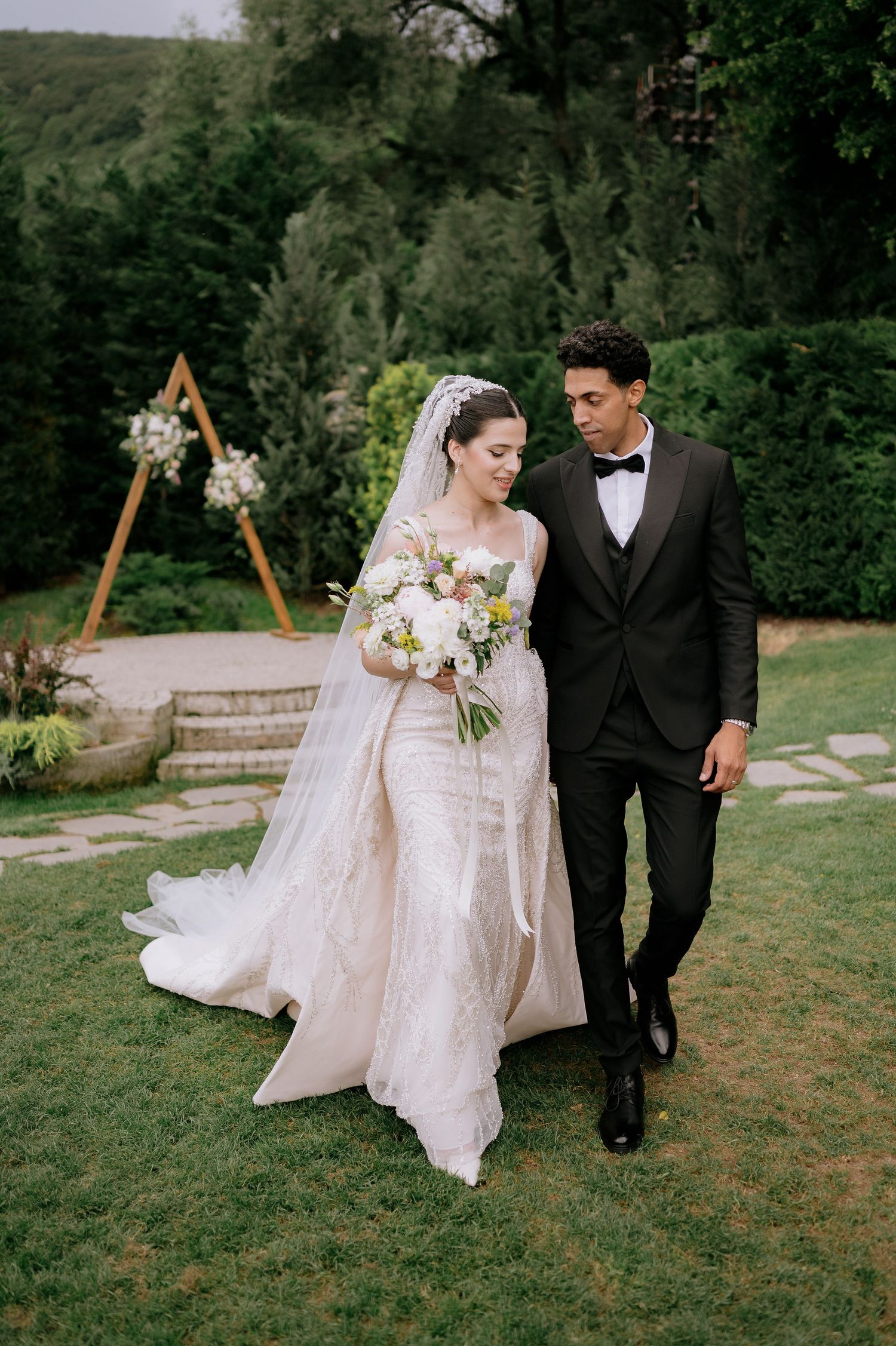 Romantic wedding portrait in garden with wooden ceremony arch visible.