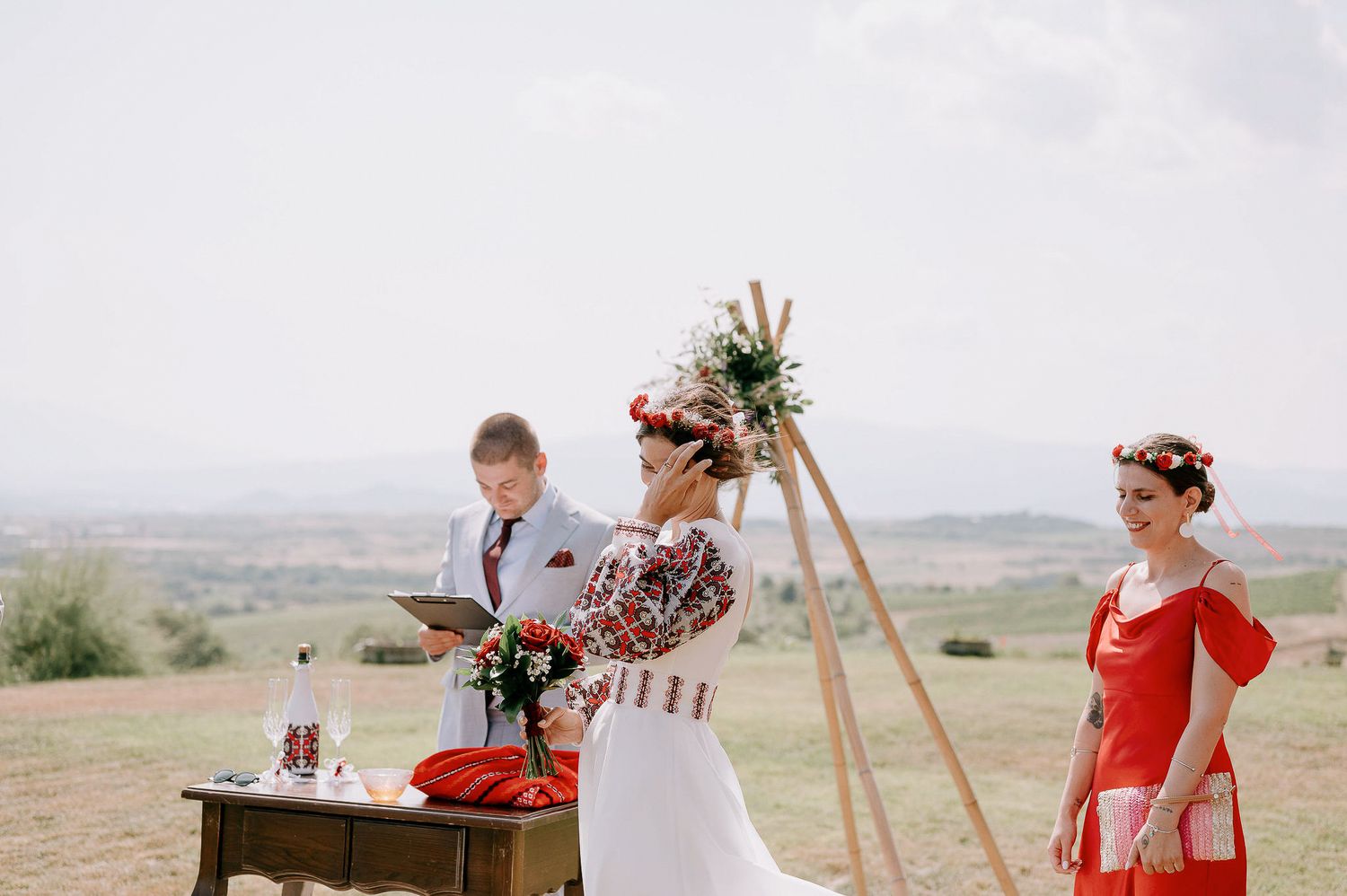 Scenic outdoor wedding ceremony with wooden benches and triangle arch overlooking valley.