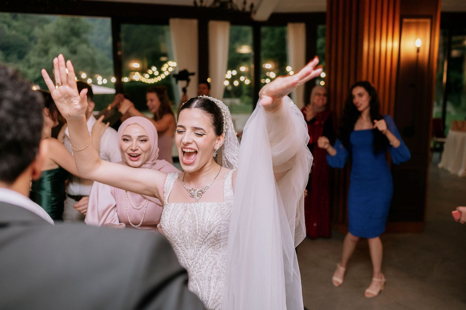 Wedding guests dancing and celebrating with raised arms at indoor reception.