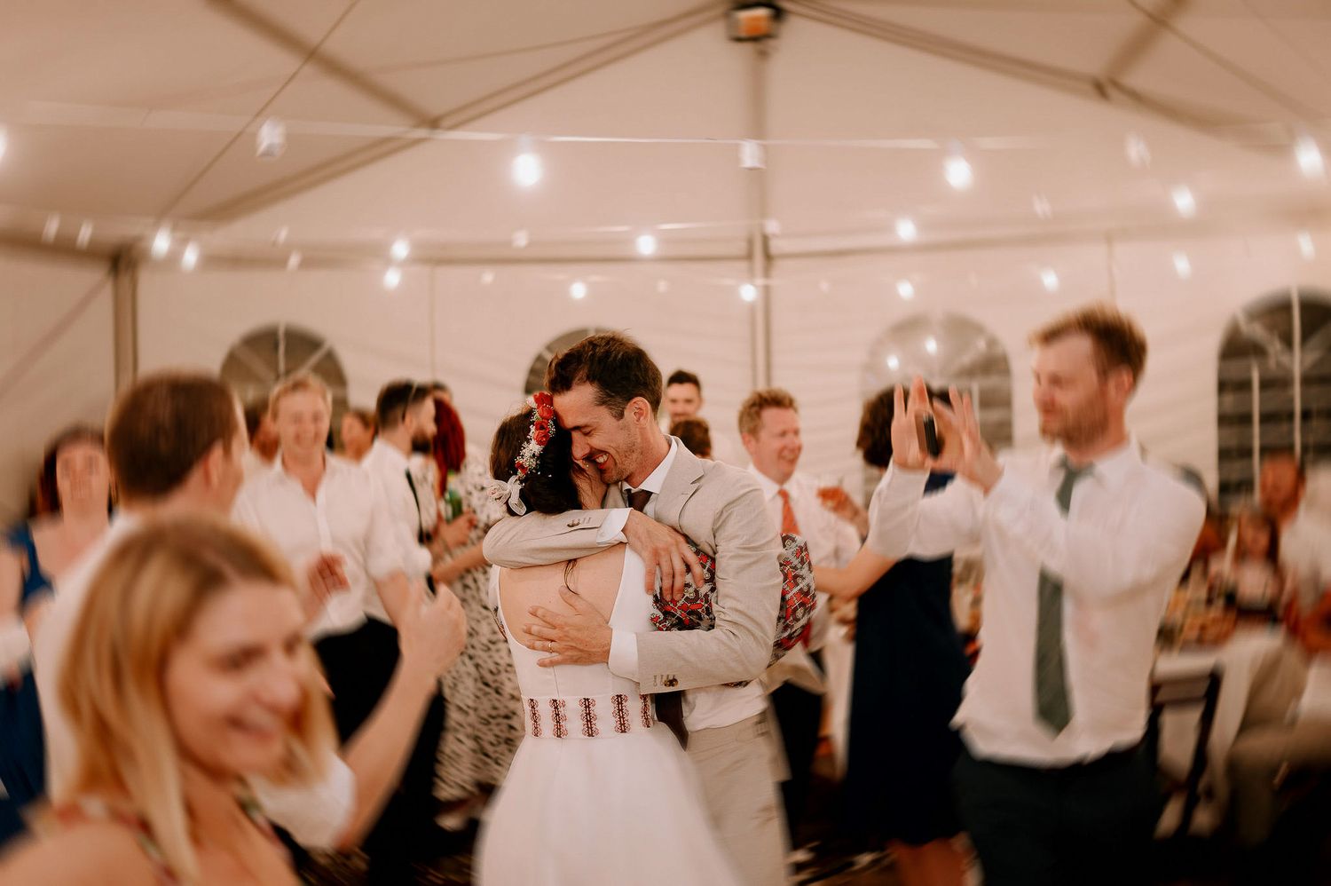 Wedding party dancing and enjoying festivities under glowing tent lights.