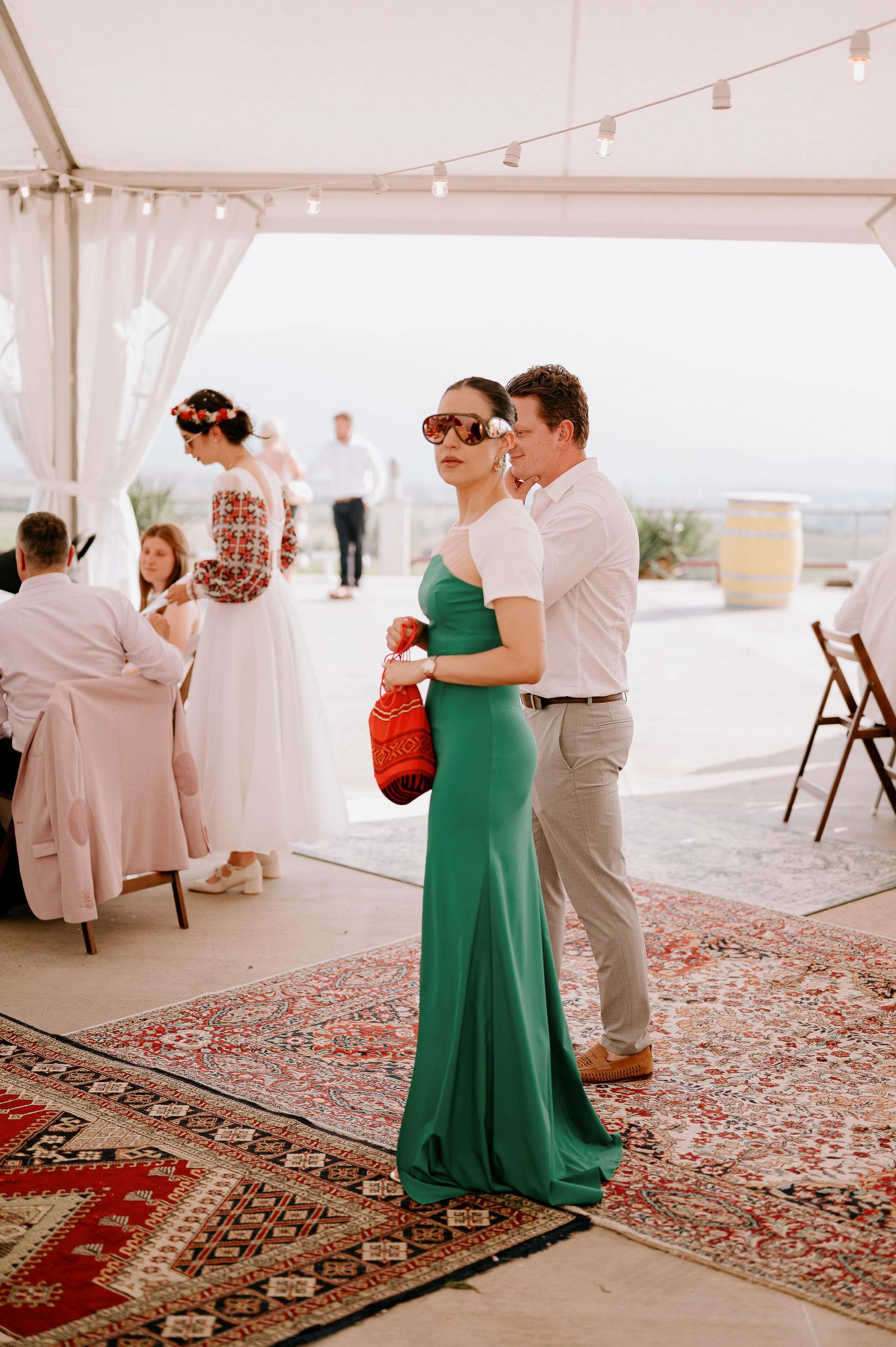 Wedding guests dance together on an ornate Persian rug under a white tent during an elegant outdoor reception.