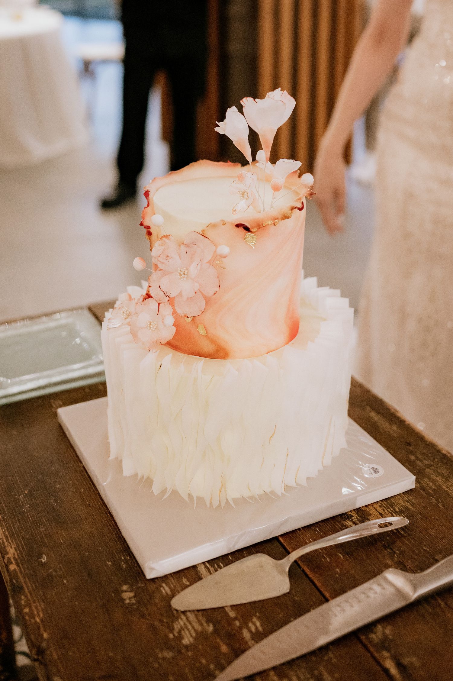 Close-up of a white wedding cake with delicate coral-colored decorative details on a wooden surface.