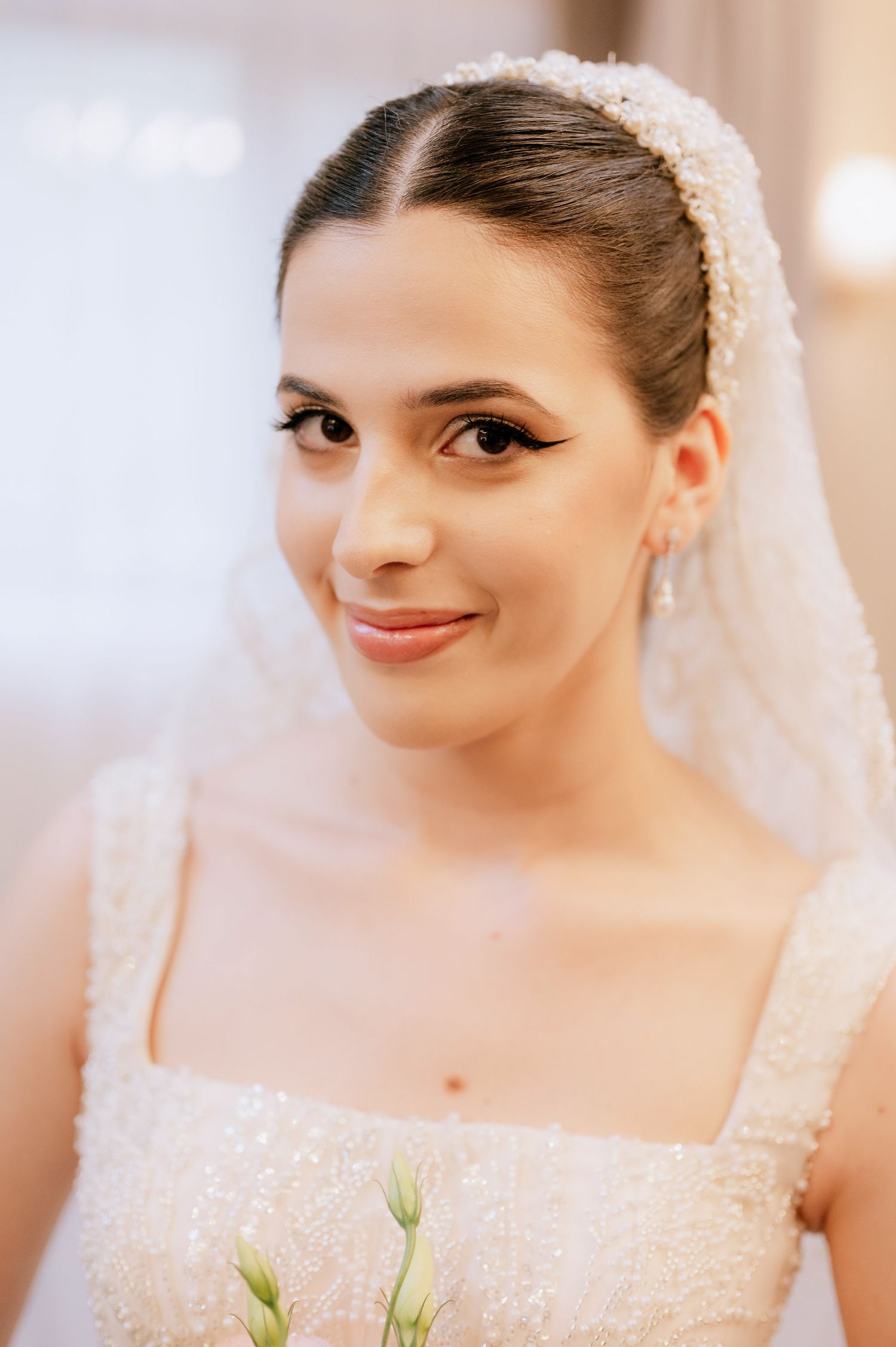 Close-up bridal portrait highlighting elegant makeup and pearl-adorned headpiece with flowing veil.