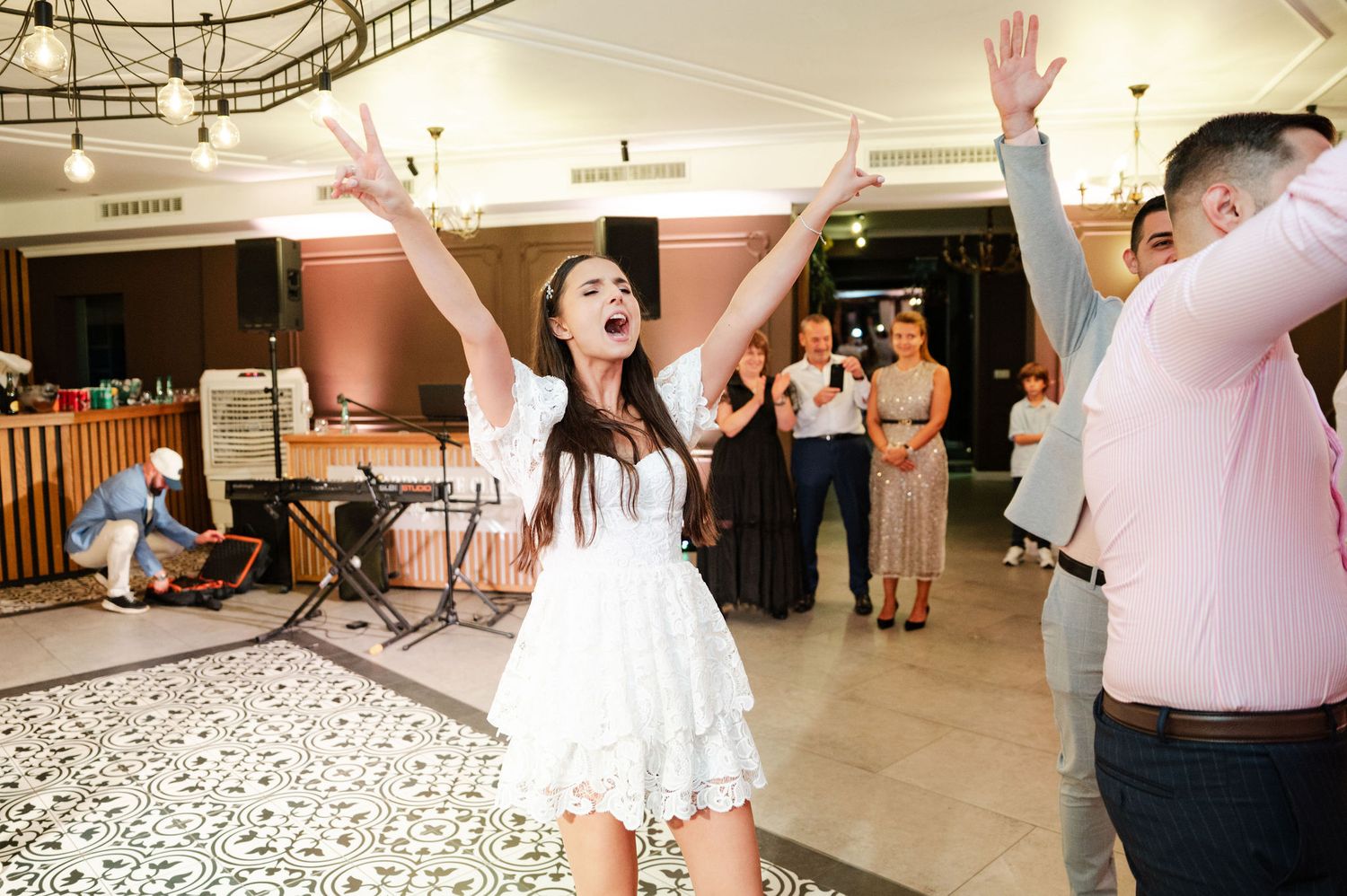 A person in a white dress jumps joyfully during a celebration in an indoor venue.