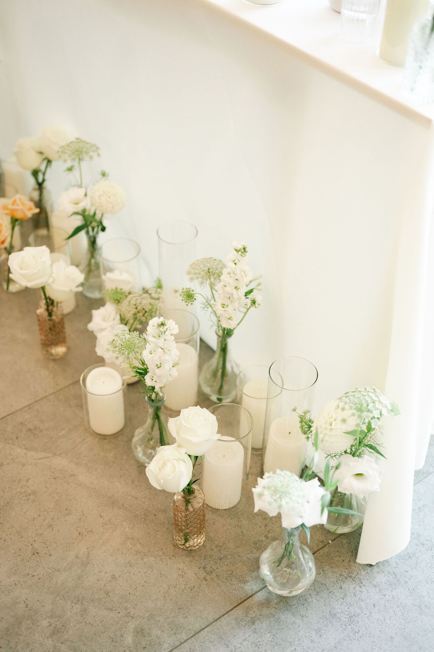 Delicate white roses and baby's breath in small glass vases arranged on concrete flooring.