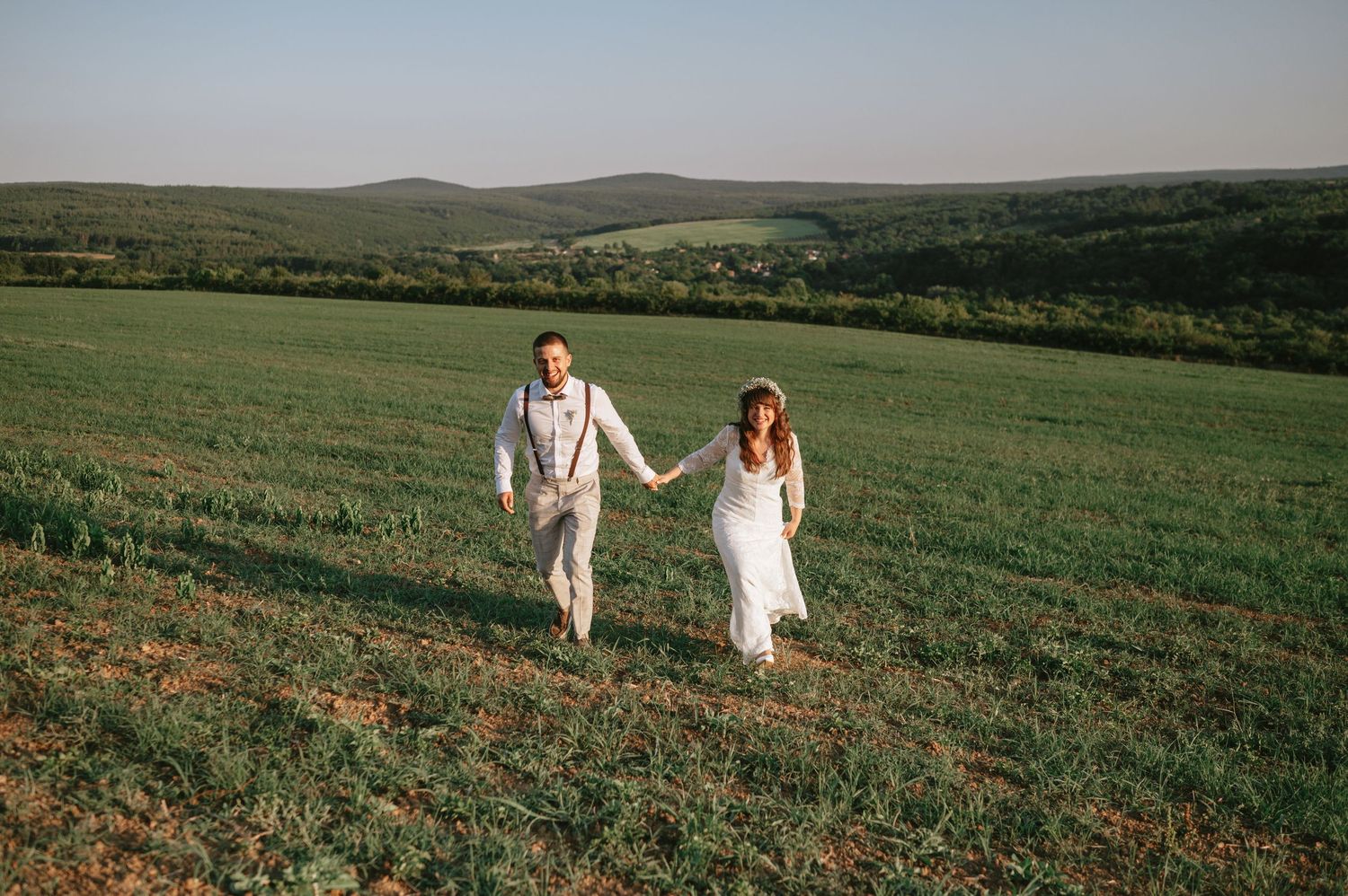 A couple walks through a rolling green meadow during their countryside wedding.