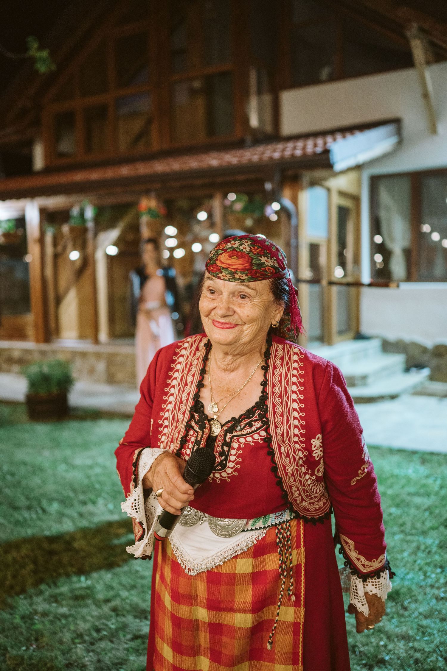 Person in traditional red and plaid folk costume smiling at outdoor event.