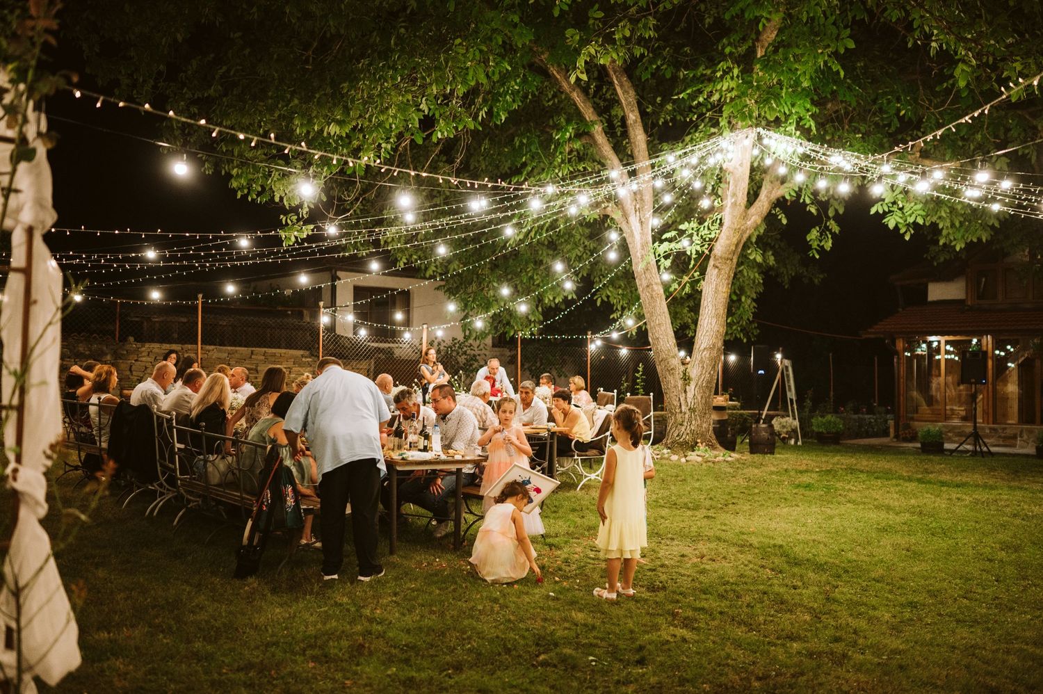 Panoramic view of a romantic outdoor wedding reception with string lights illuminating the garden.