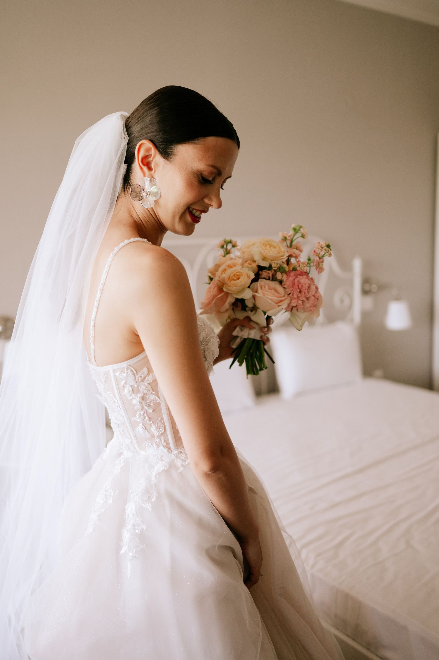 Candid moment of bride in lace gown with flowing veil against neutral background.