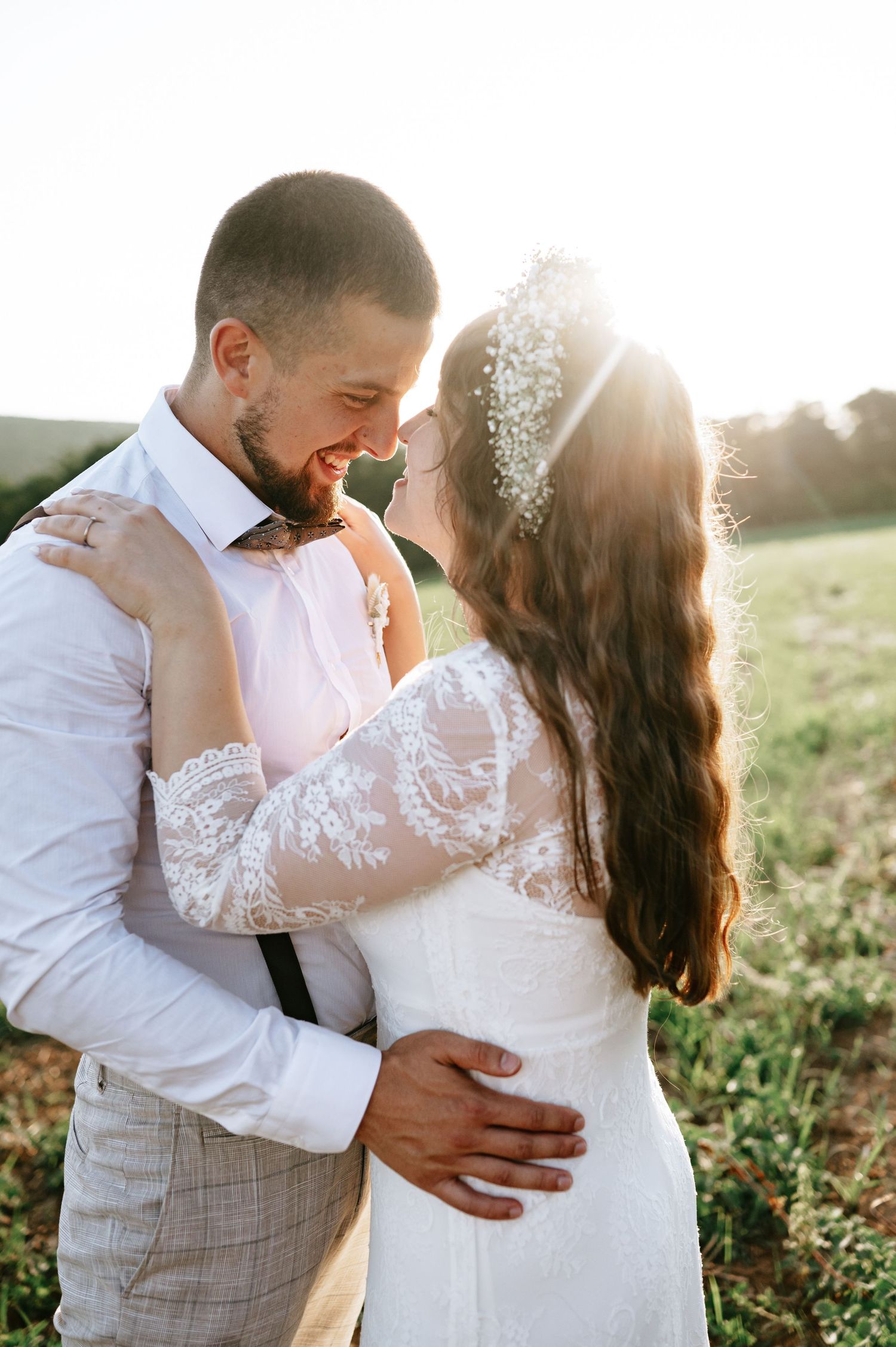 A loving couple shares an intimate moment in a sunlit field wearing wedding attire.