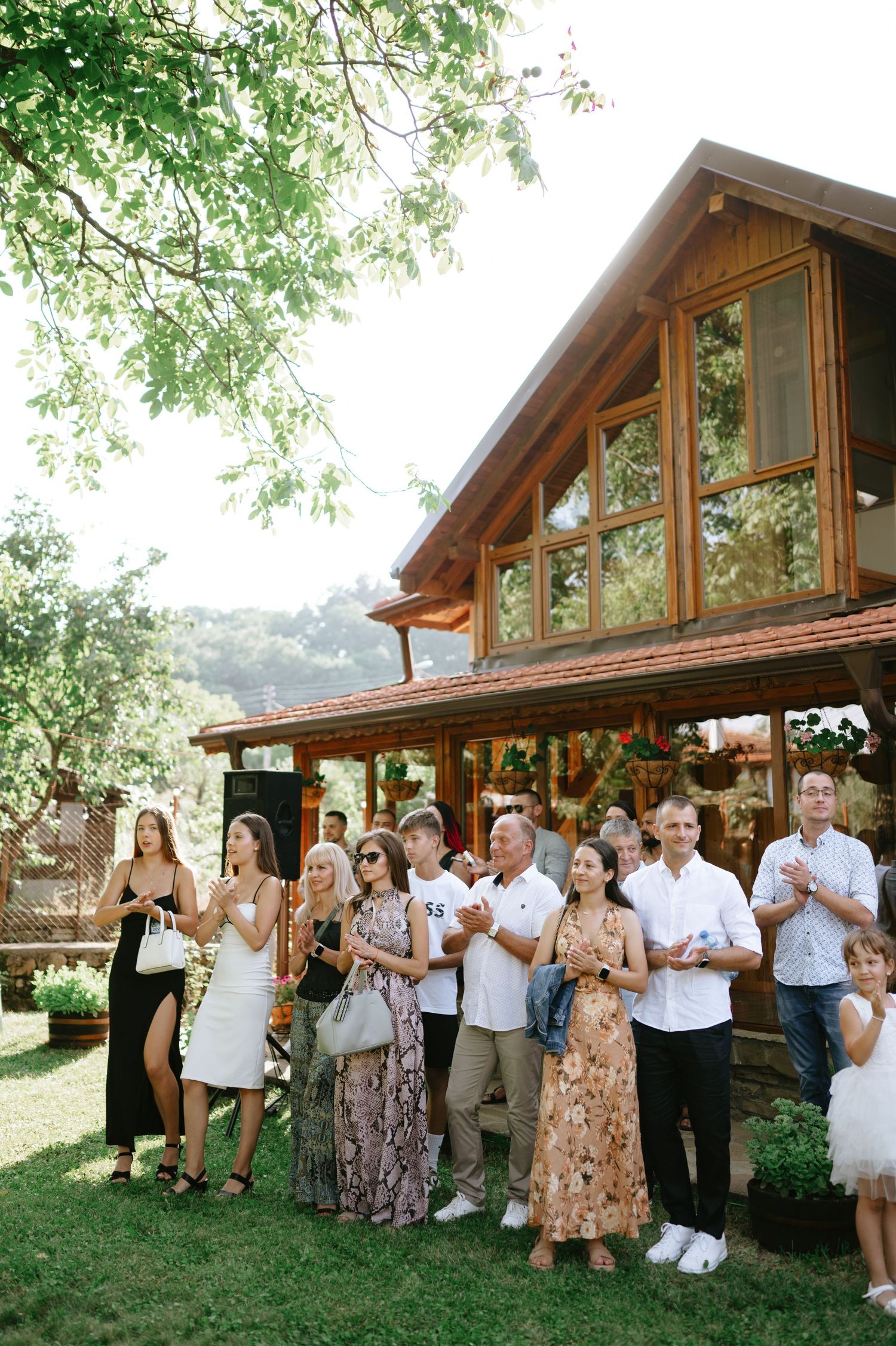 Wedding guests applauding during an outdoor celebration at a wooden lodge venue.