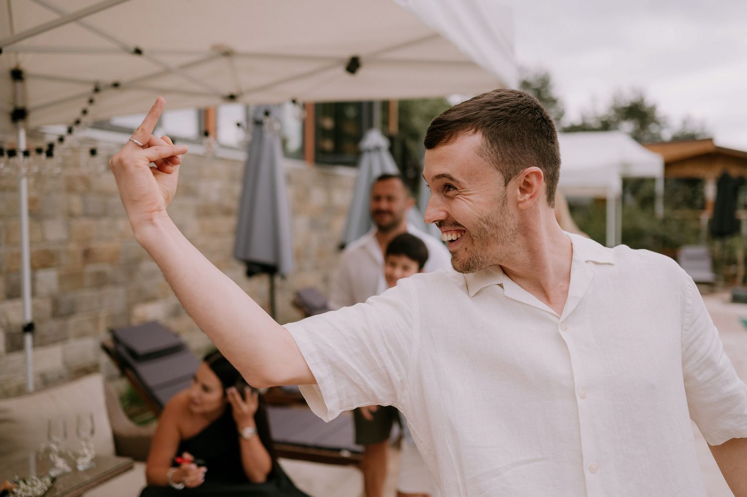 Wedding guests dance and celebrate outdoors under a white tent canopy.
