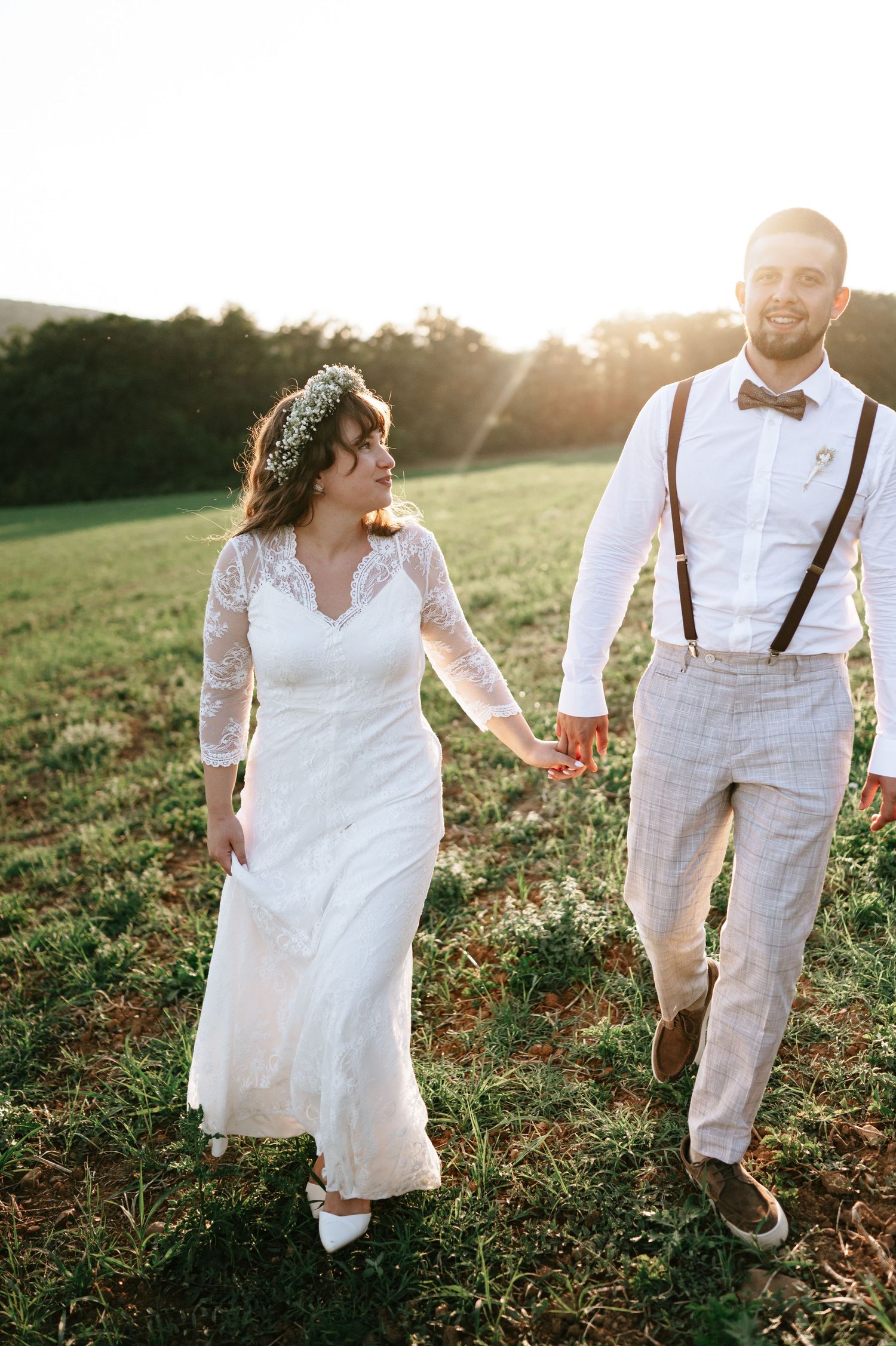 Playful wedding couple dancing in field during sunset photoshoot.