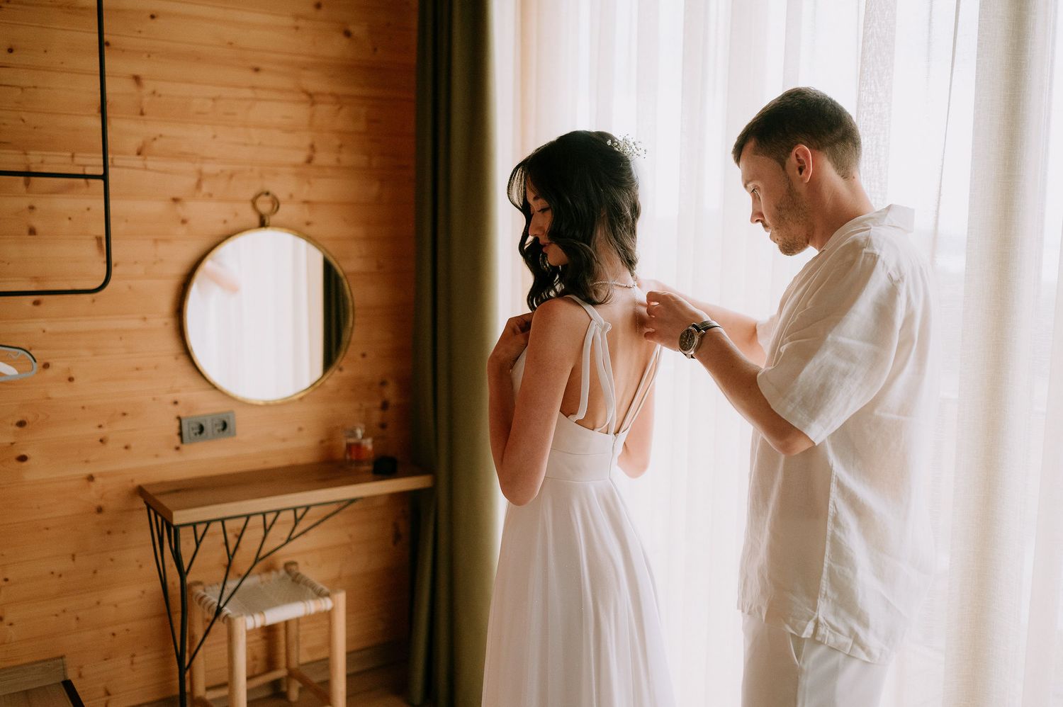 Natural light streaming through white curtains in rustic wooden room.