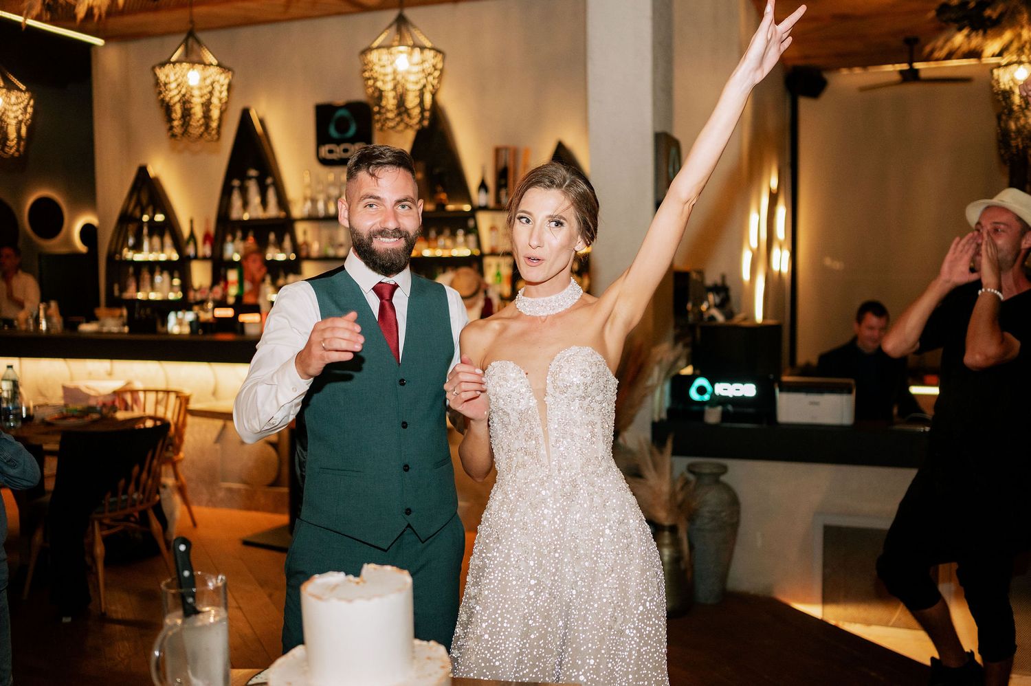 A couple celebrates with champagne next to their wedding cake in an intimate venue setting.