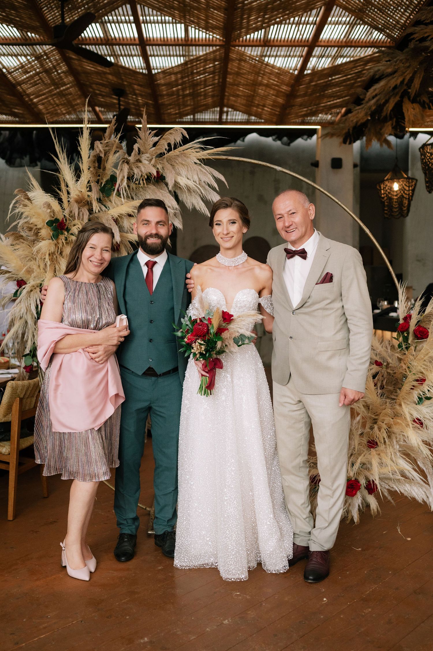 Elegant wedding photo with dried pampas grass arch and burgundy floral accents in a rustic venue.
