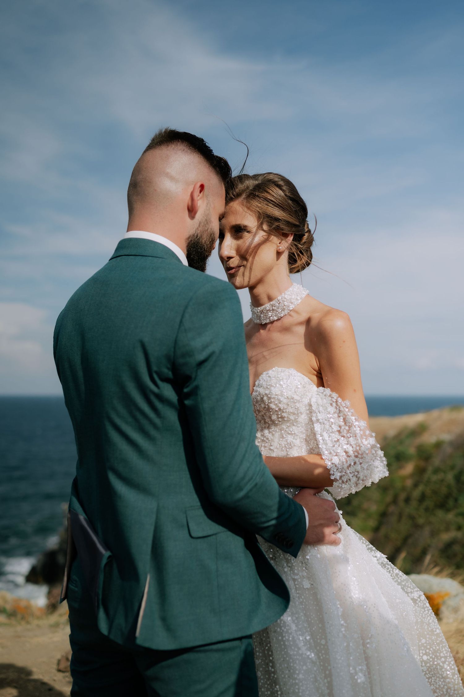 A romantic wedding portrait session on a cliff with the ocean horizon in the background.