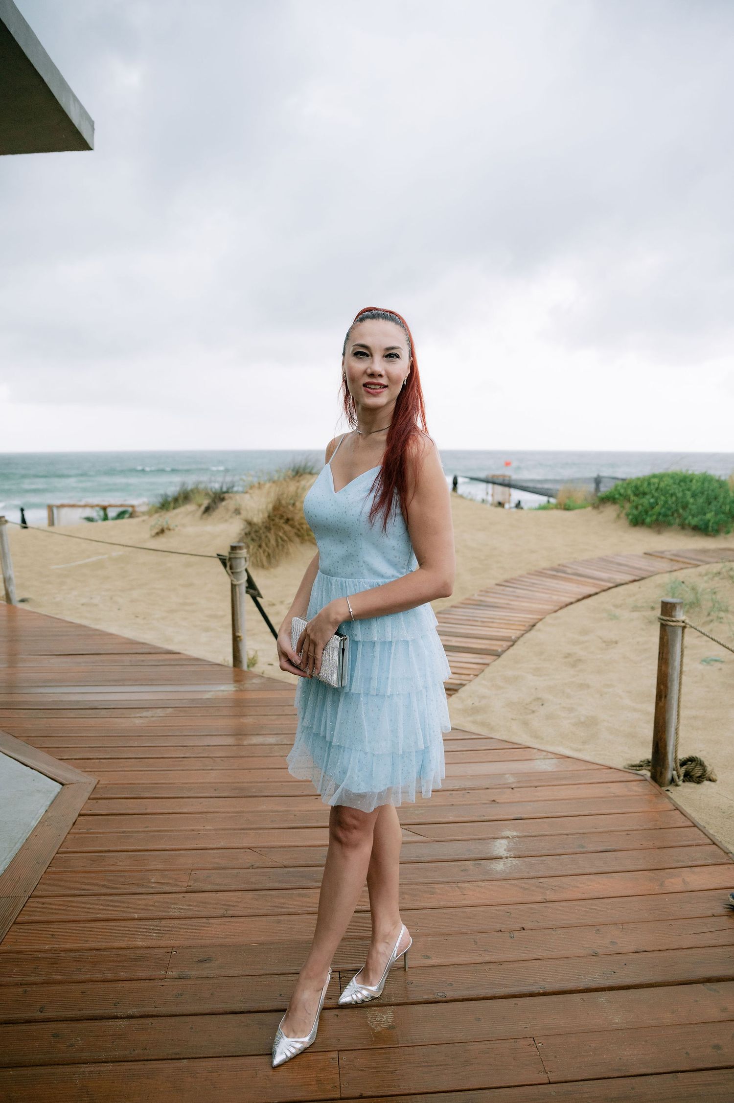 Woman in light blue dress twirling on wooden boardwalk by the beach.