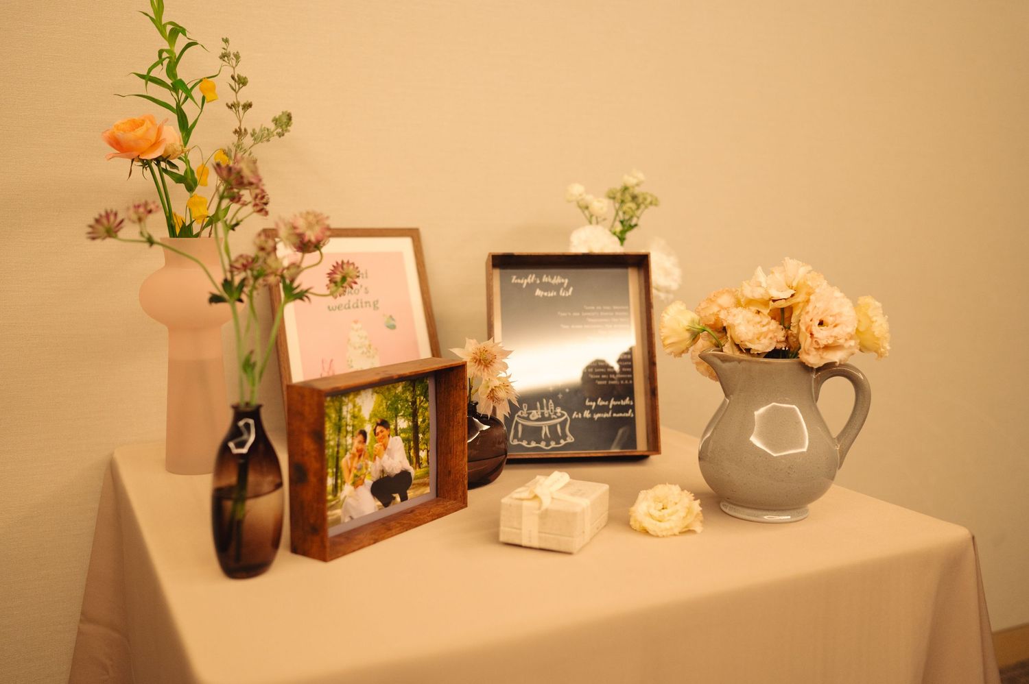 Decorative display table with flowers, vases and small ornaments against a beige wall.